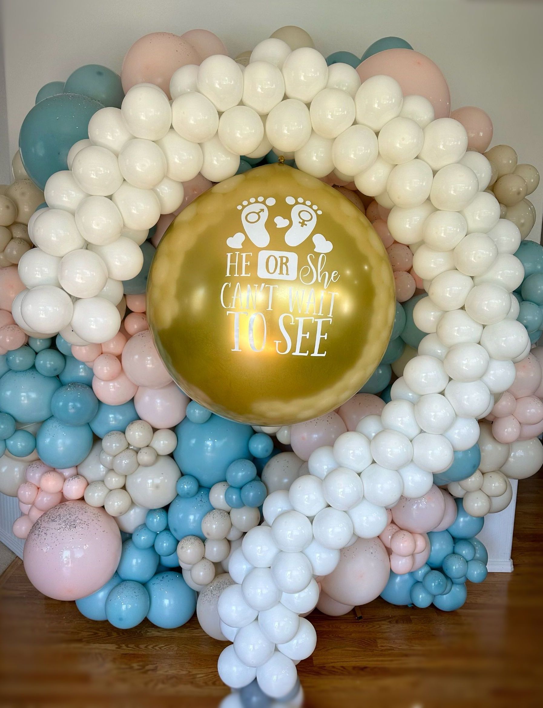 Balloon arch in pastel colors for a baby shower; includes a gold balloon with text.