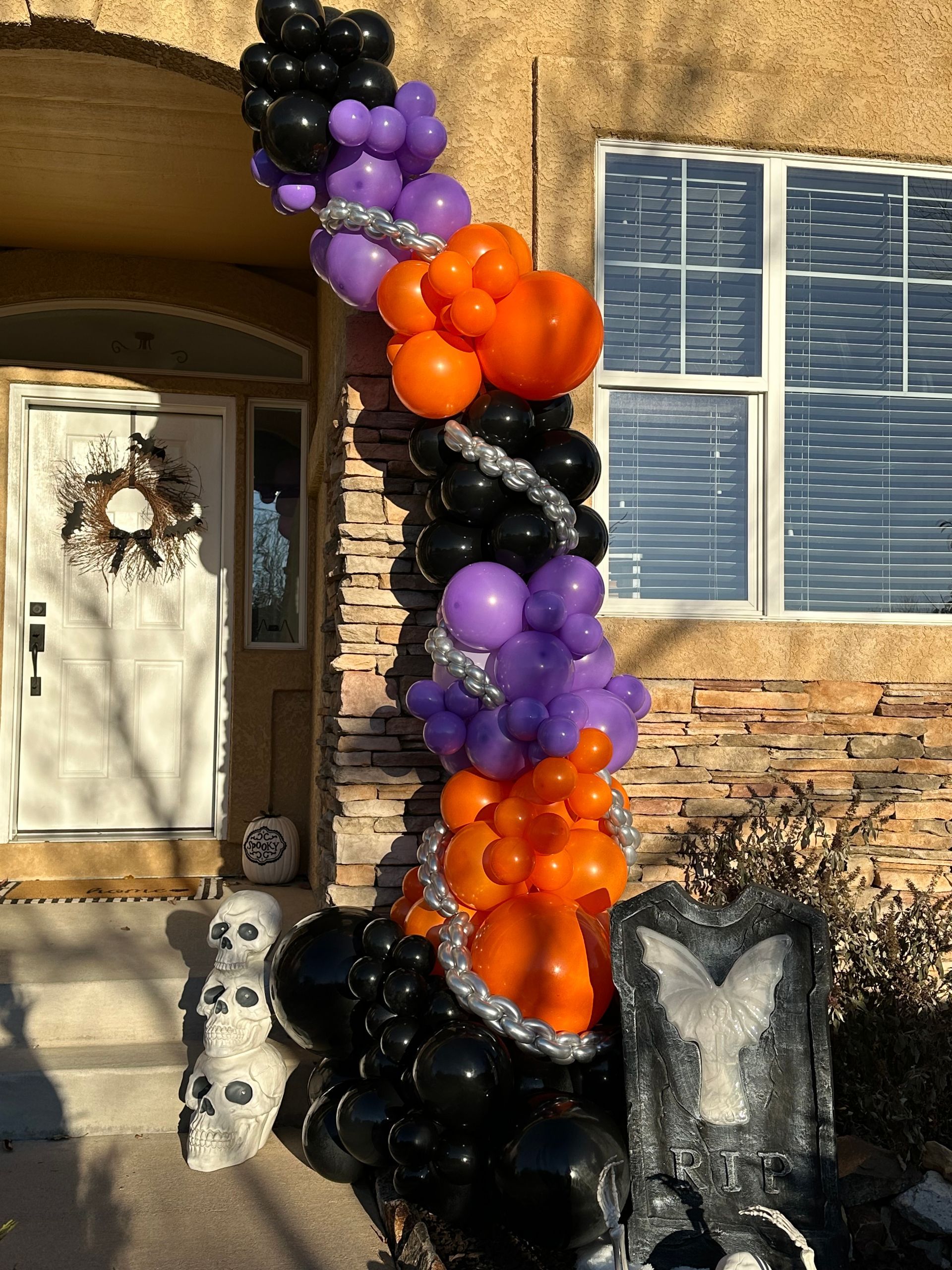 Halloween balloon decoration with black, purple, and orange balloons around a pillar.