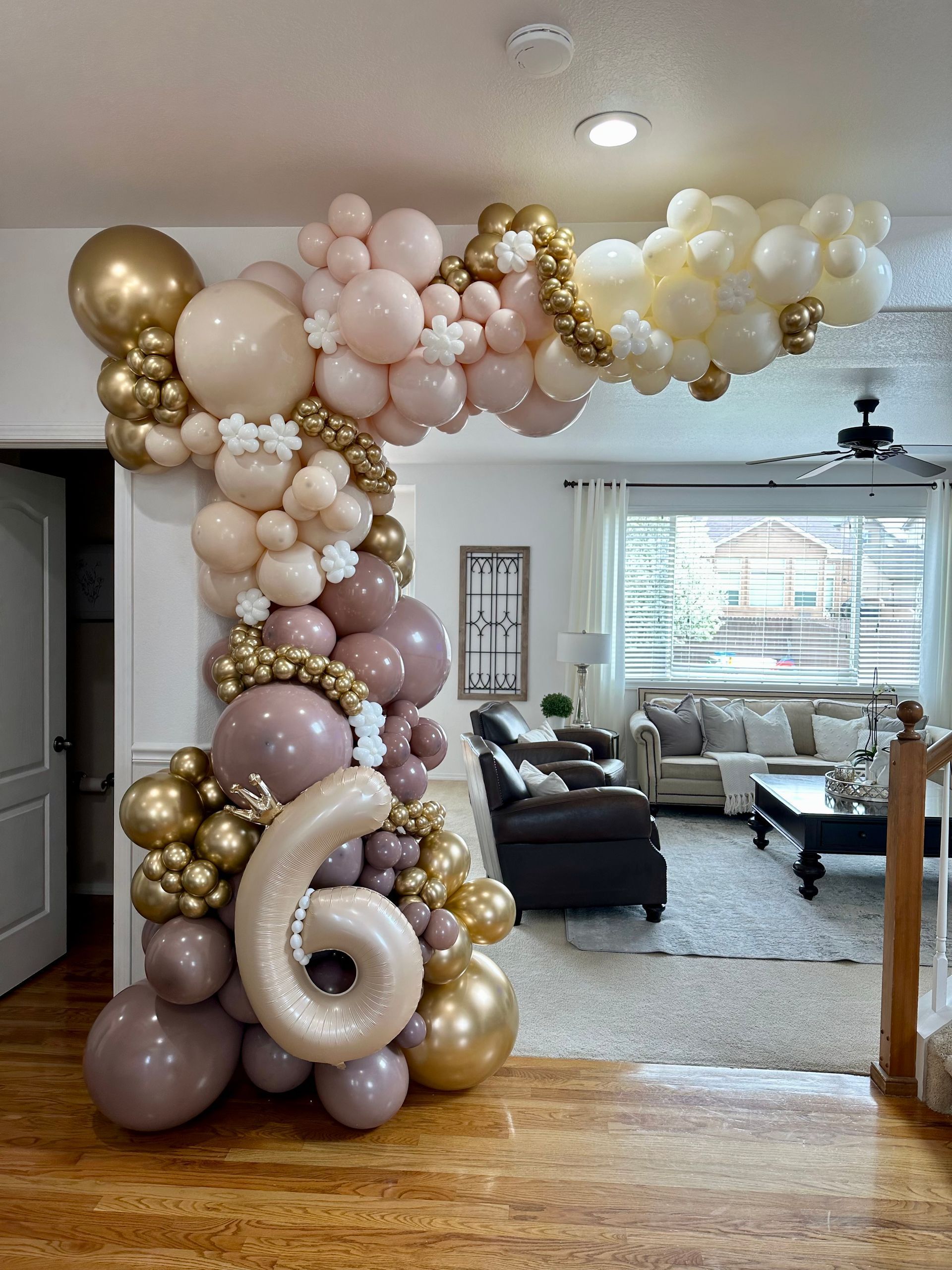 Balloon arch with pink, gold, and cream balloons framing a doorway, with a number 6 balloon.