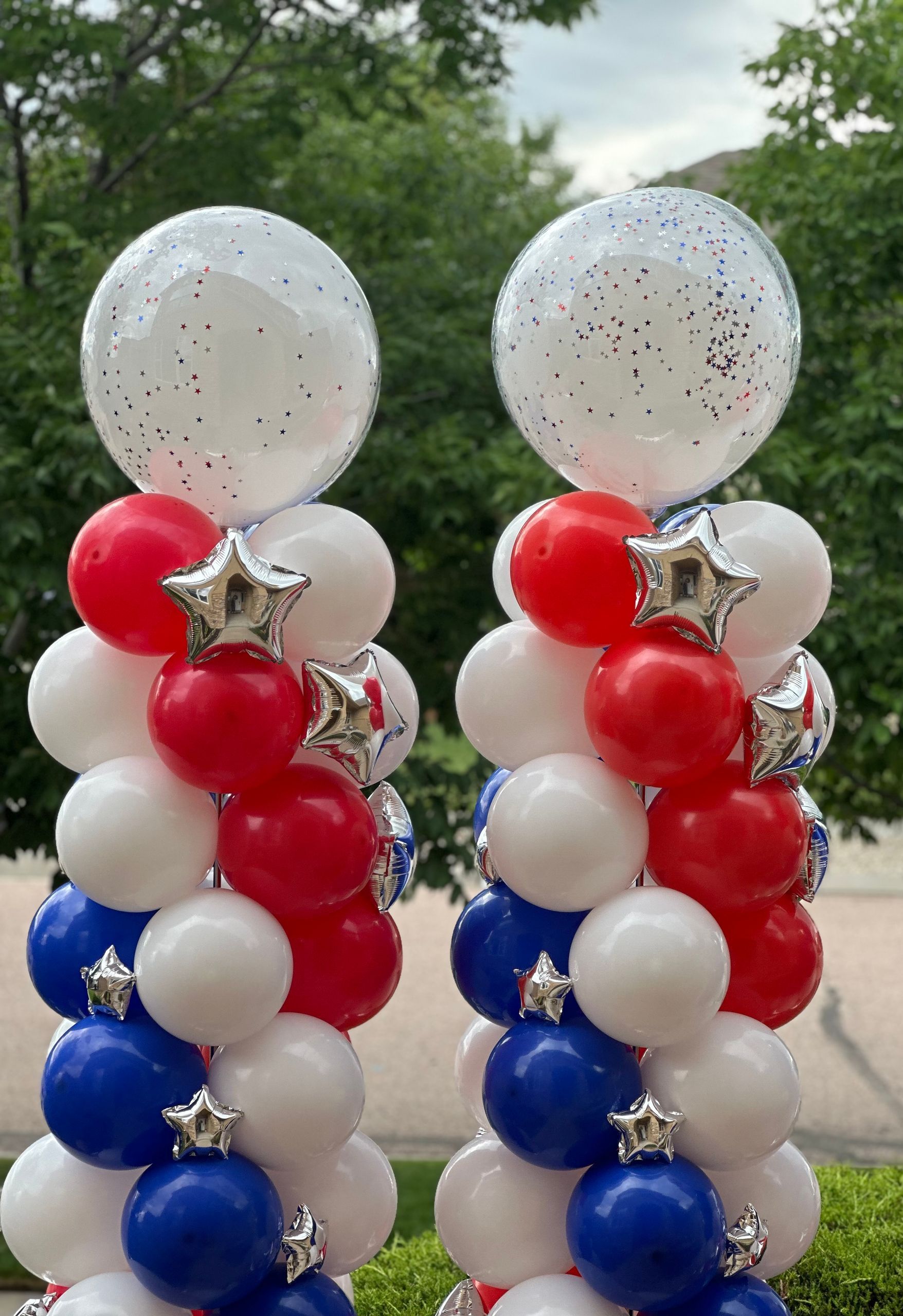 Two patriotic balloon columns; red, white, and blue balloons with silver star accents and clear confetti-filled toppers.