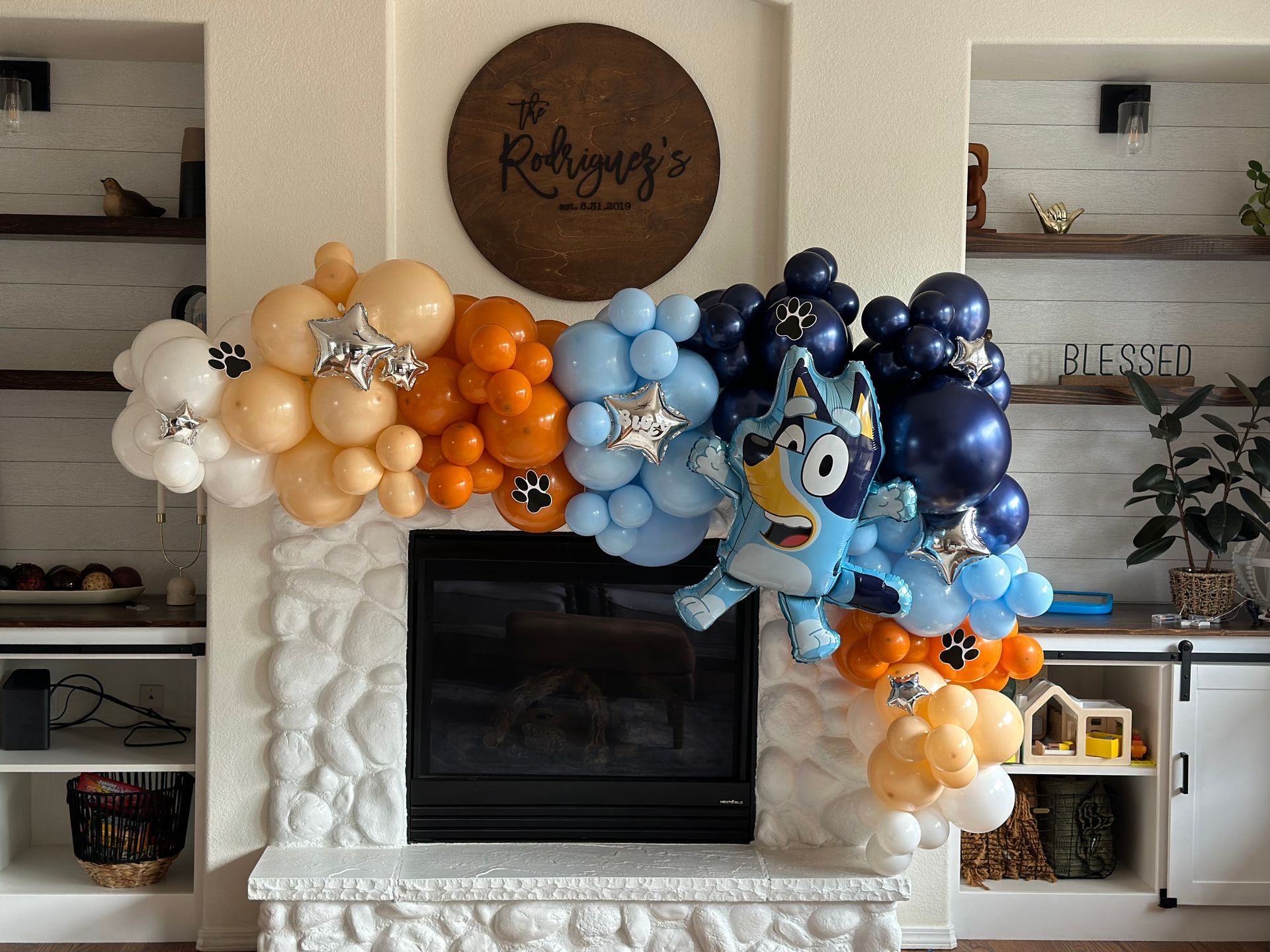 Balloon arch over a fireplace, with Bluey character, various colors: blue, orange, tan, white.
