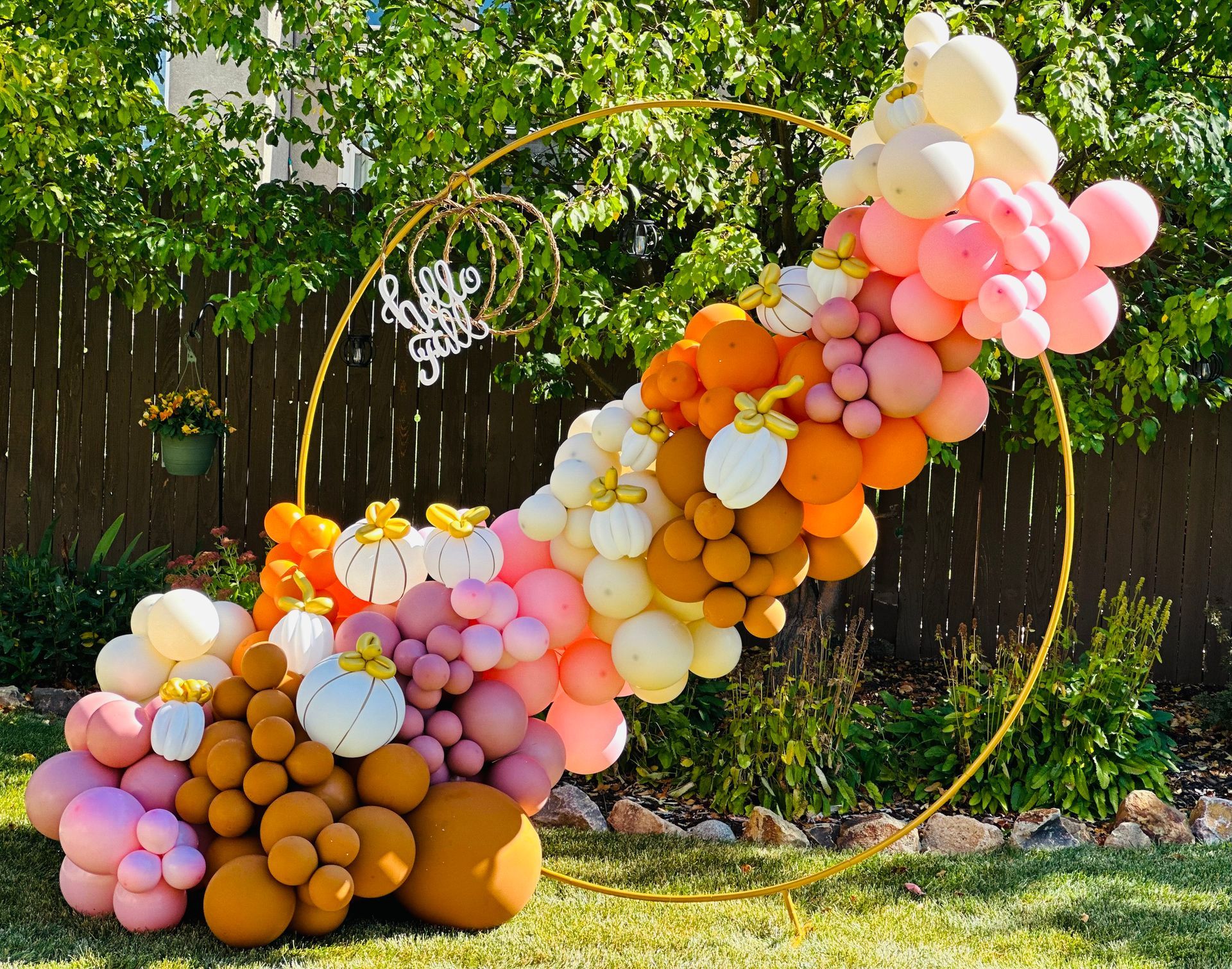A gold hoop decorated with an ombre balloon arch in shades of orange, pink, and white, with small pumpkin accents.