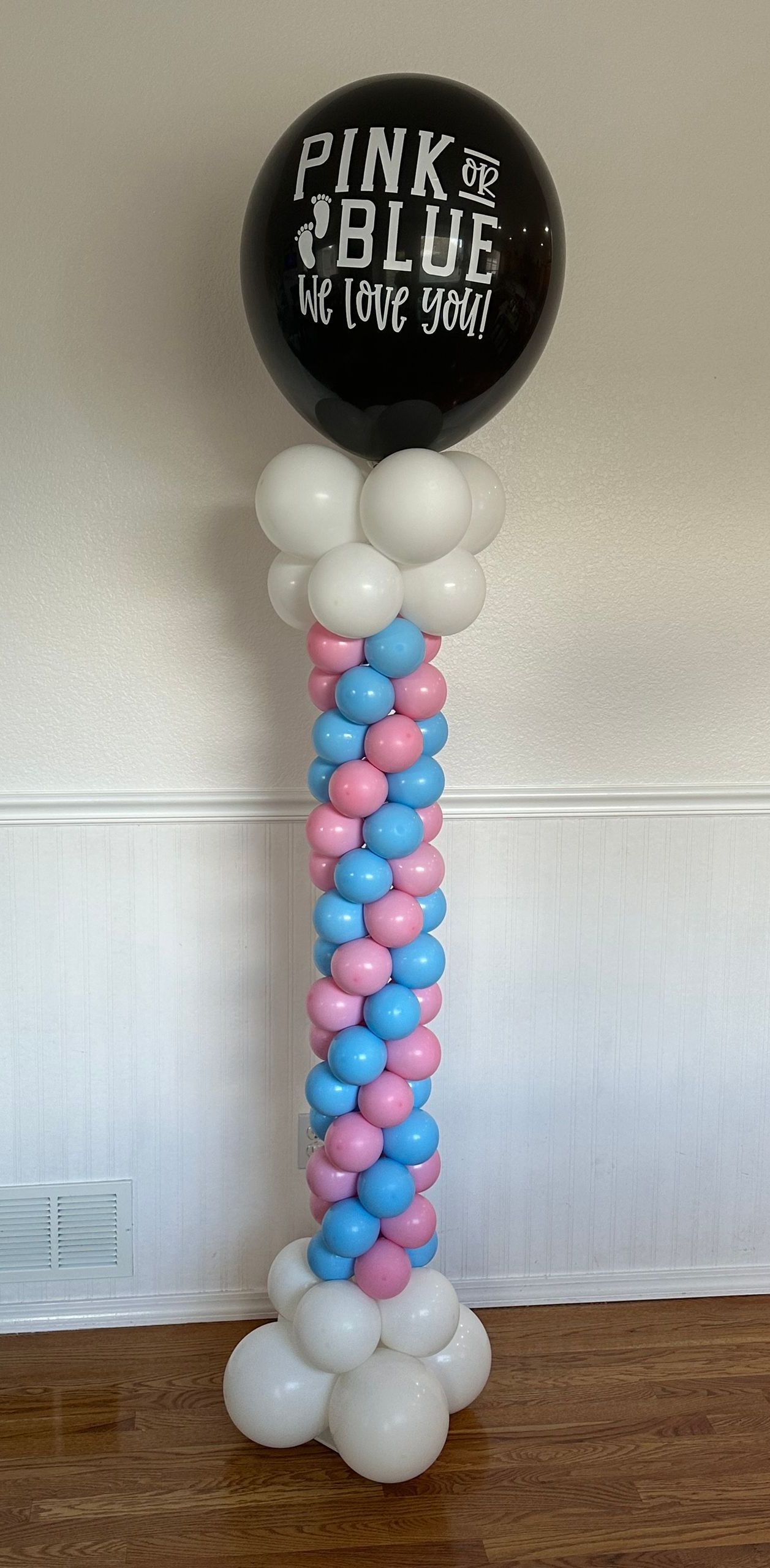 A balloon column with pink and blue balloons supporting a black balloon that says