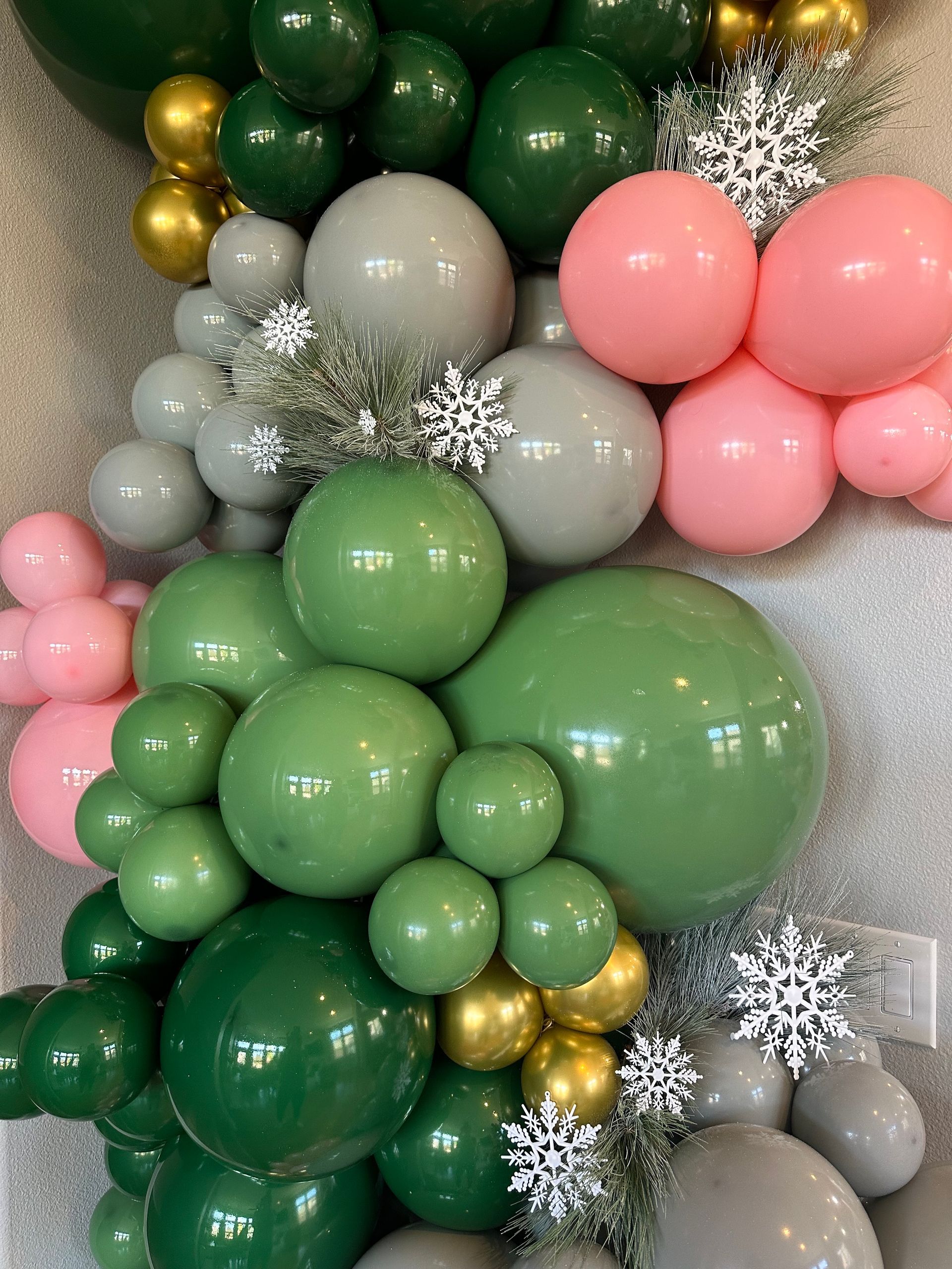 Balloon arch in various shades of green, pink, gray, and gold, with silver snowflakes.