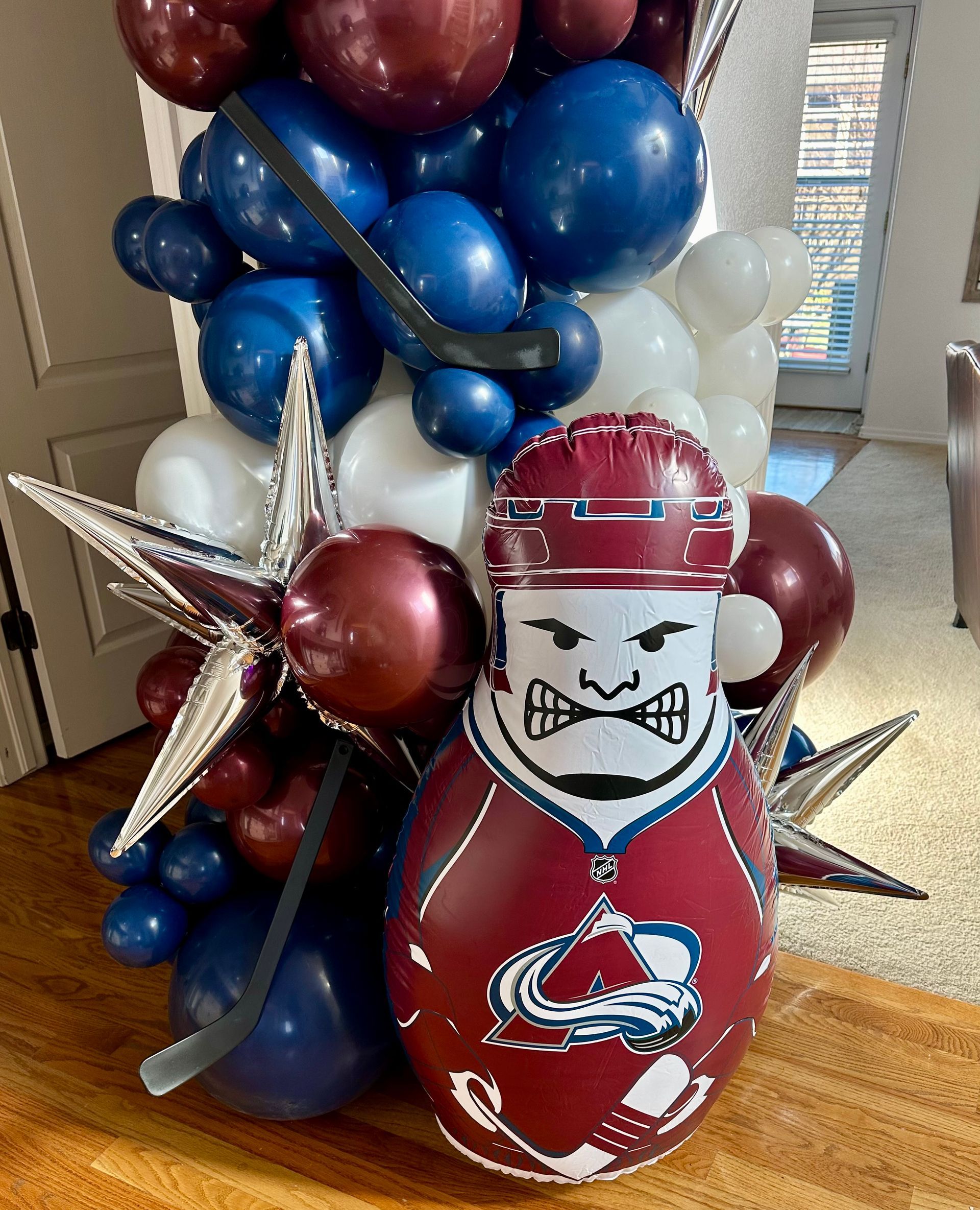 A balloon arrangement with an Avalanche hockey player in front of blue, white, and maroon balloons.