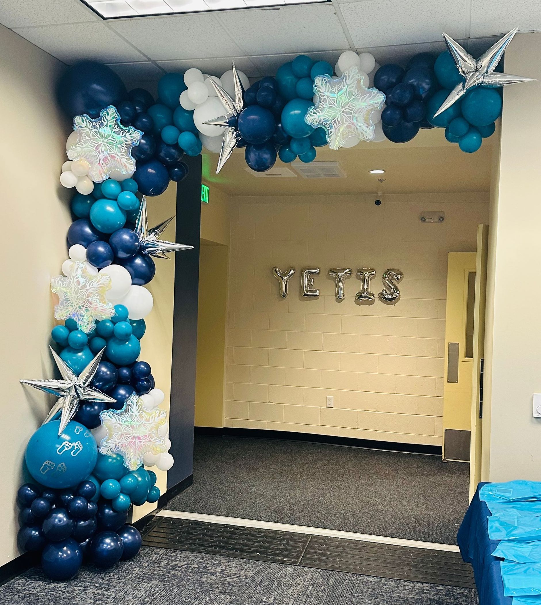 Balloon archway decorated with snowflakes and teal, white, and navy balloons leads to a room labeled