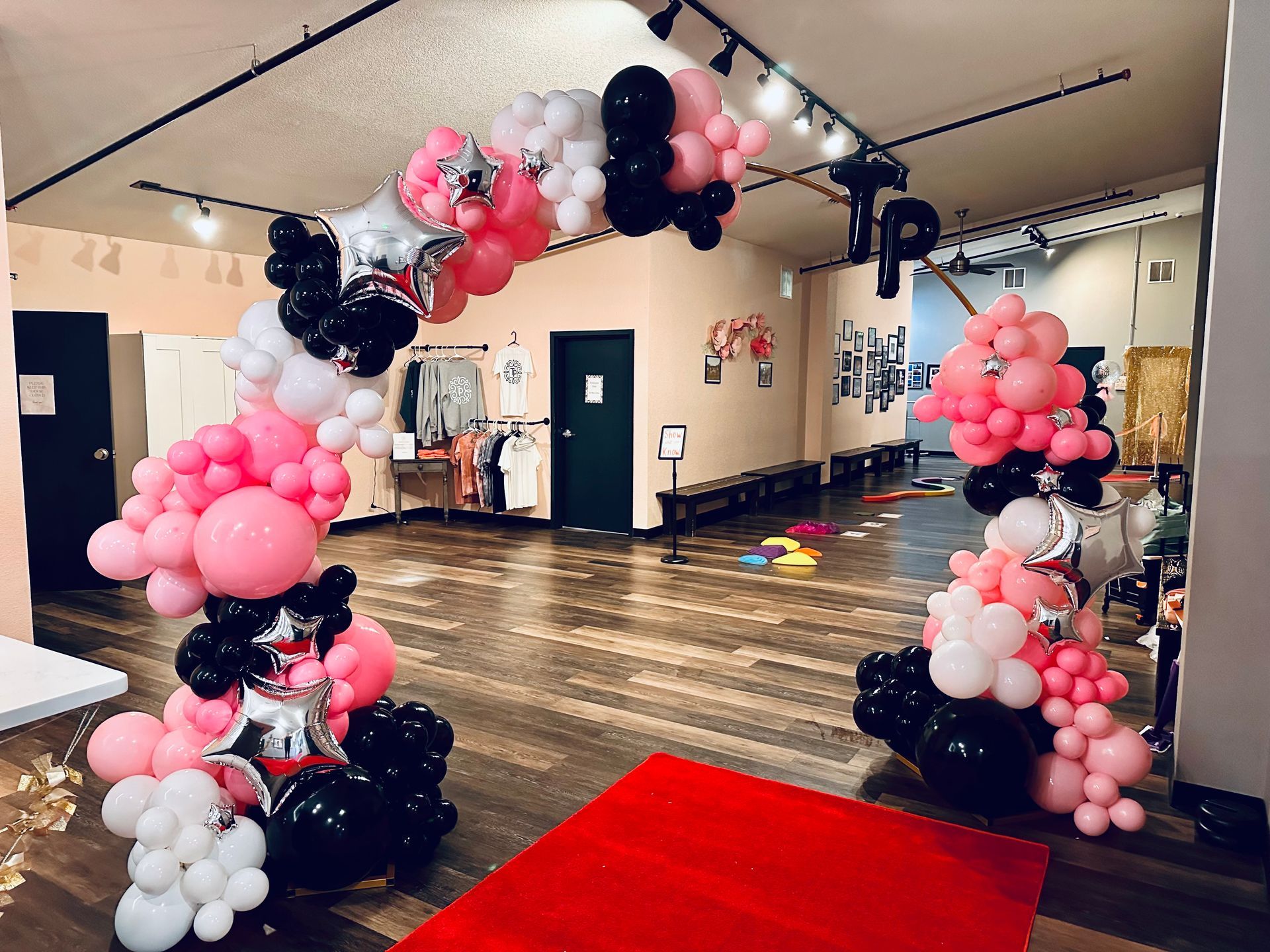 Balloon arch entrance to a room; pink, black, white balloons and a red carpet.