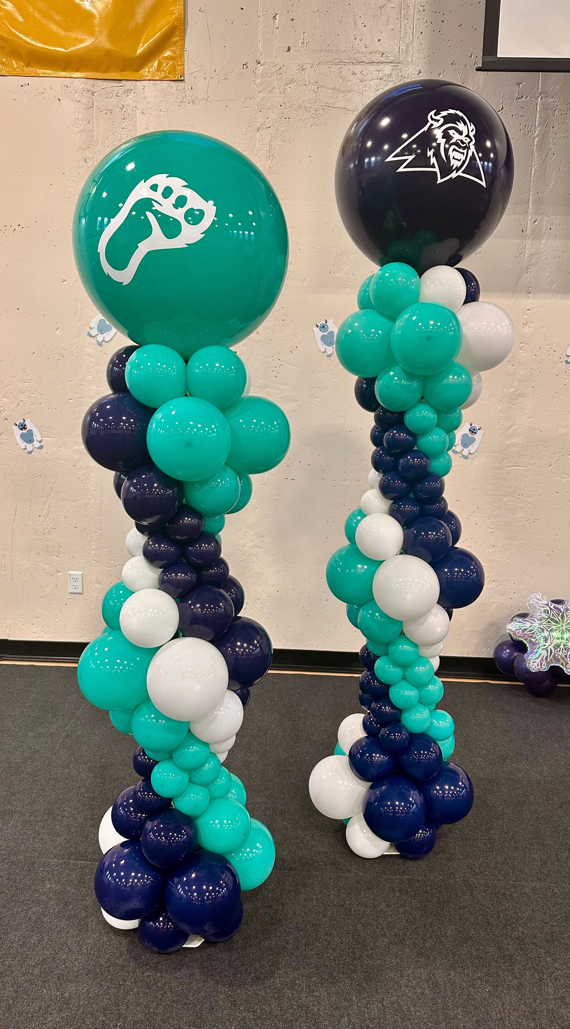 Two teal, white, and navy balloon columns with top spheres, one with a footprint.