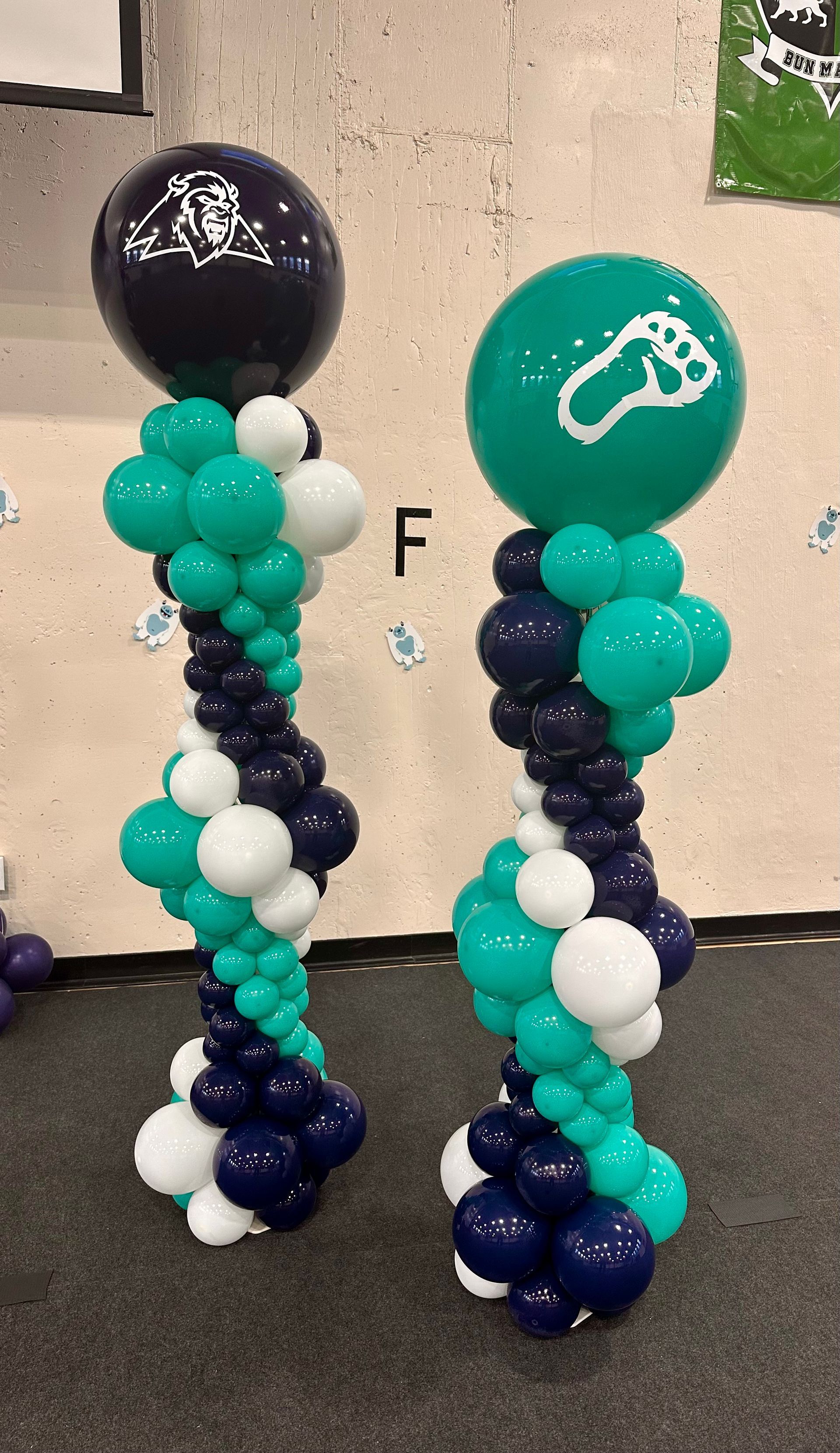 Two balloon columns: navy, teal, and white spiral design, topped with navy and teal balloons with a logo.