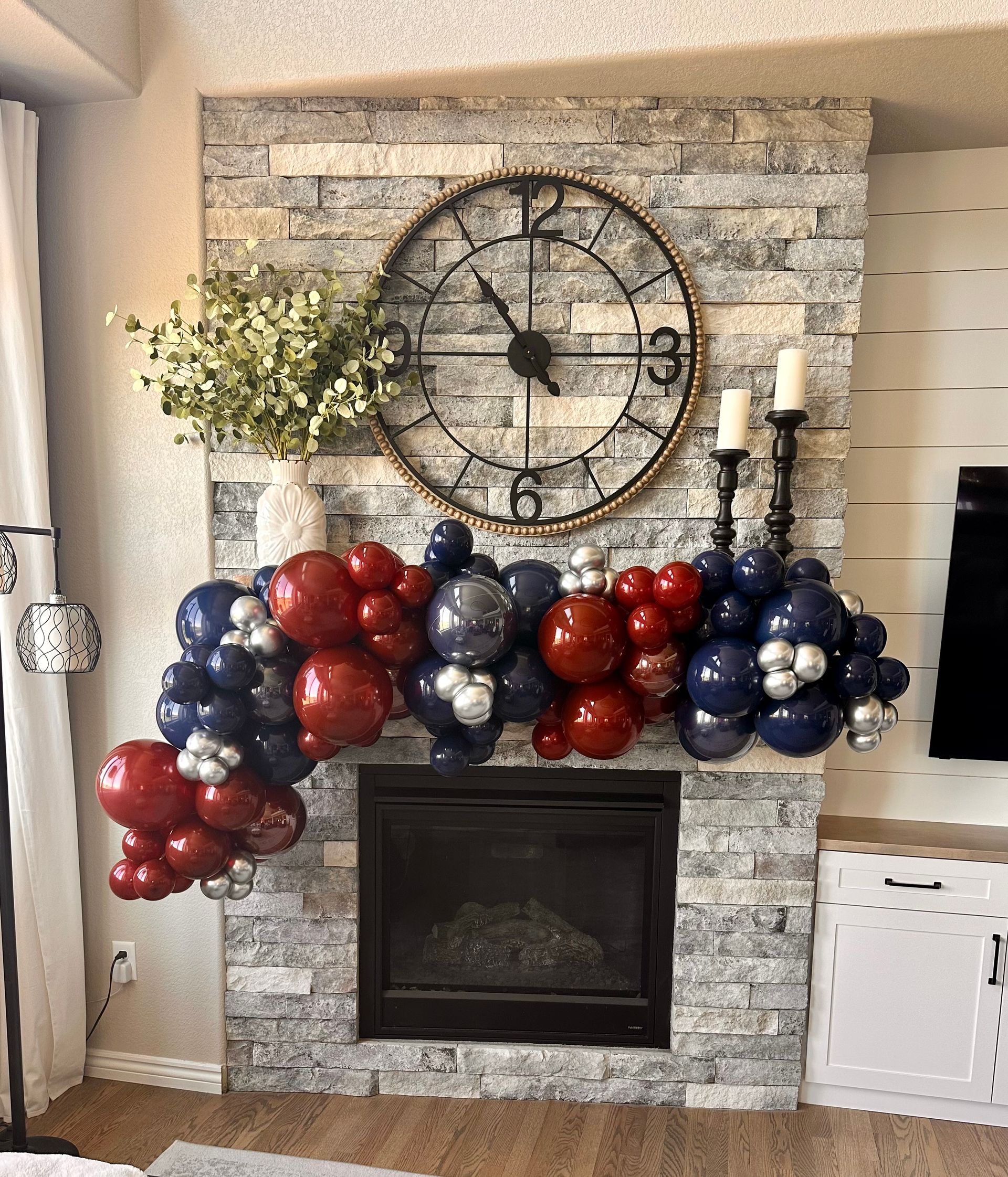 Fireplace decorated with red, blue, and silver balloons; clock, candles, and greenery.