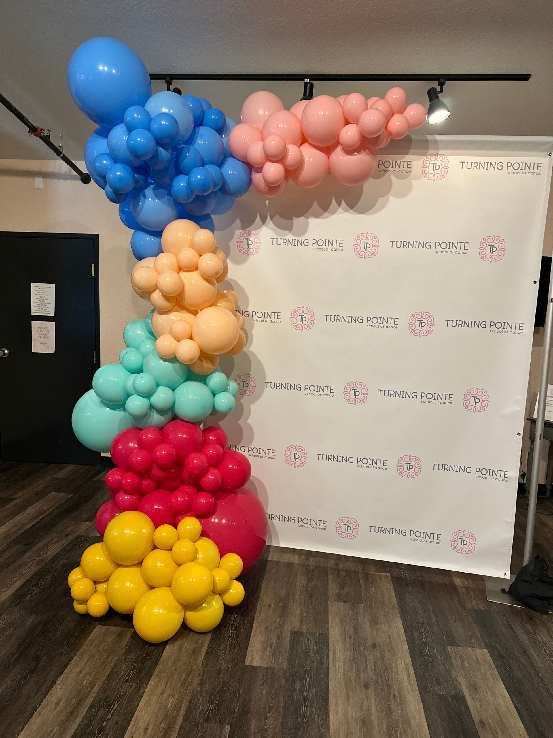 Colorful balloon column display beside a white backdrop in a room.