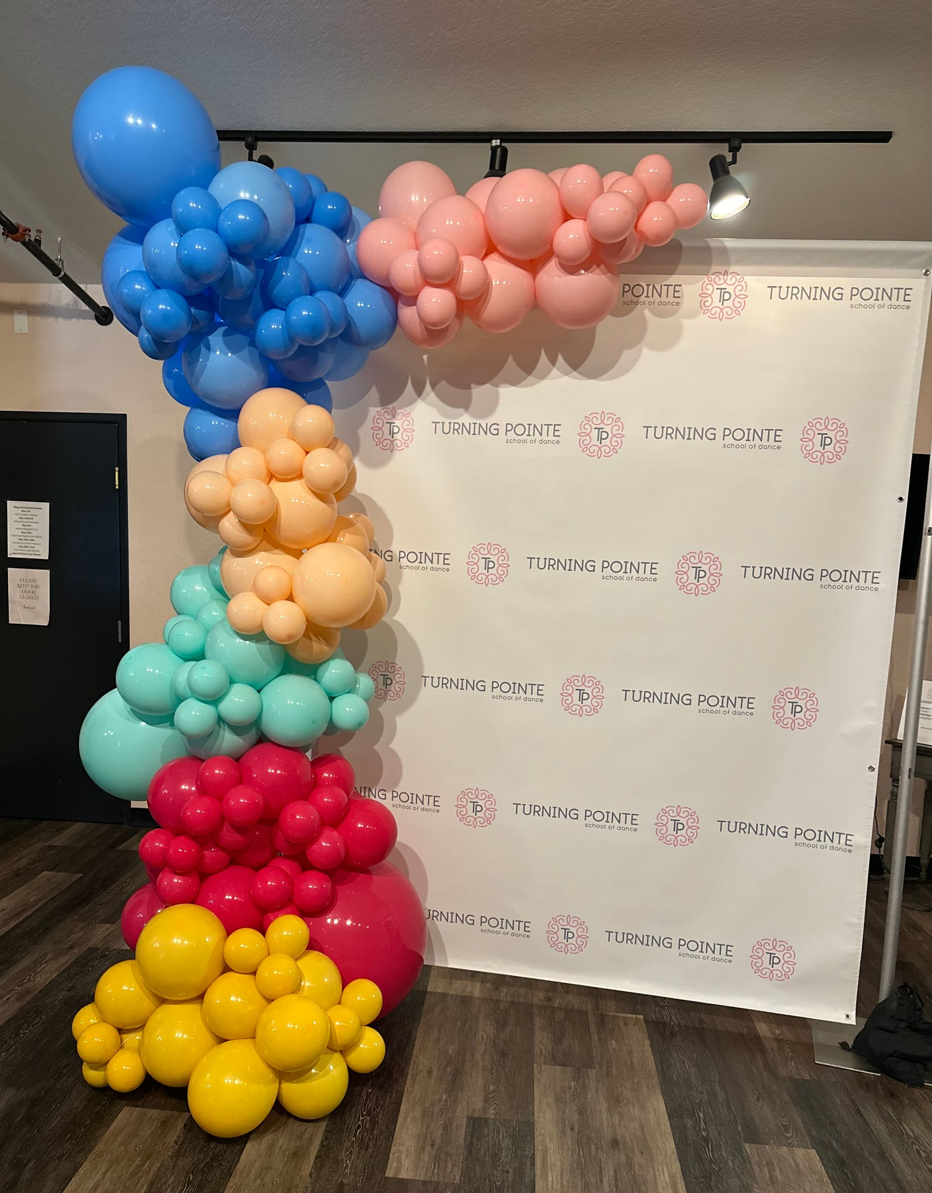 Colorful balloon arrangement beside a white backdrop in a room.
