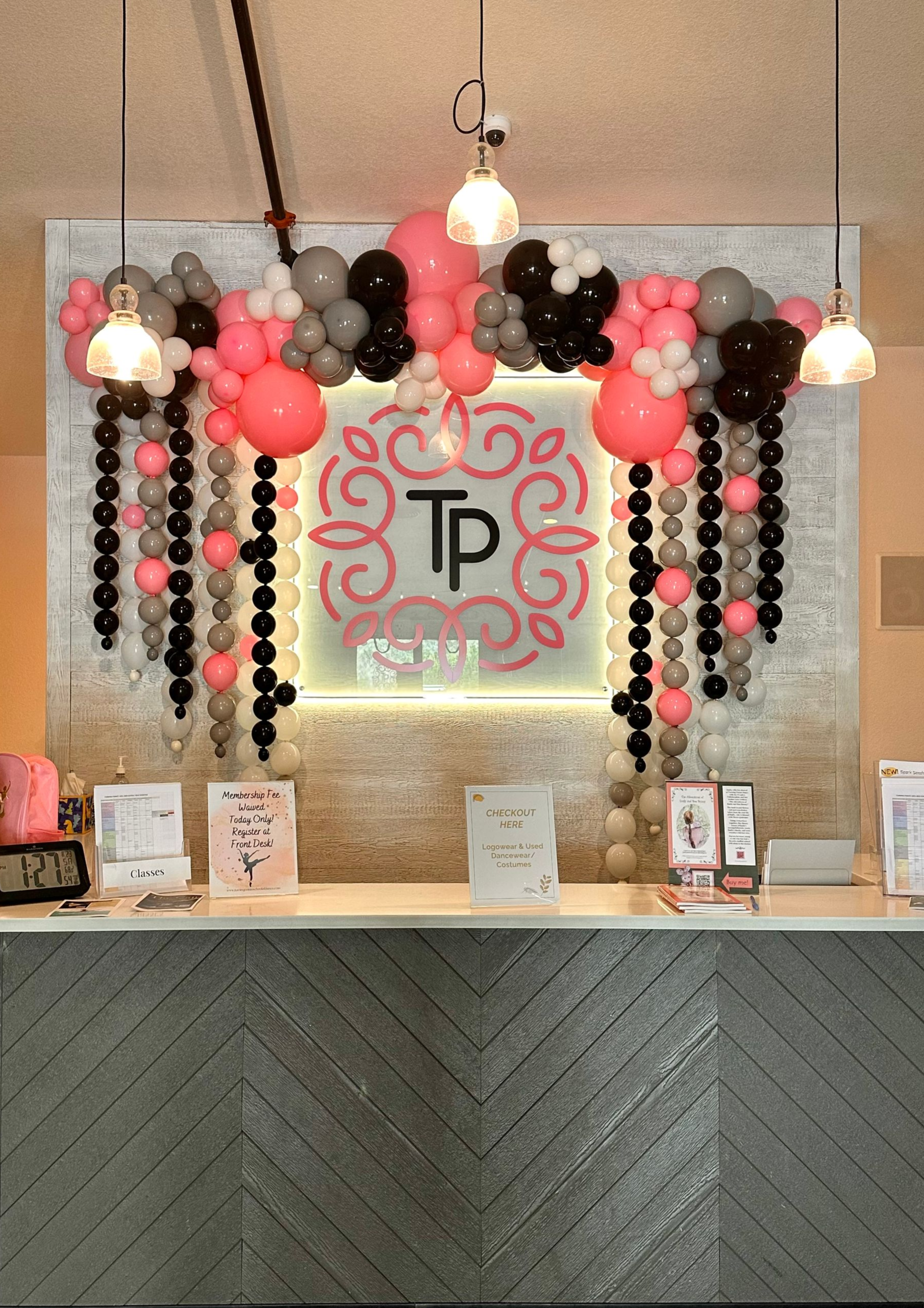 Reception desk with pink, black, and gray balloon arch. The sign reads