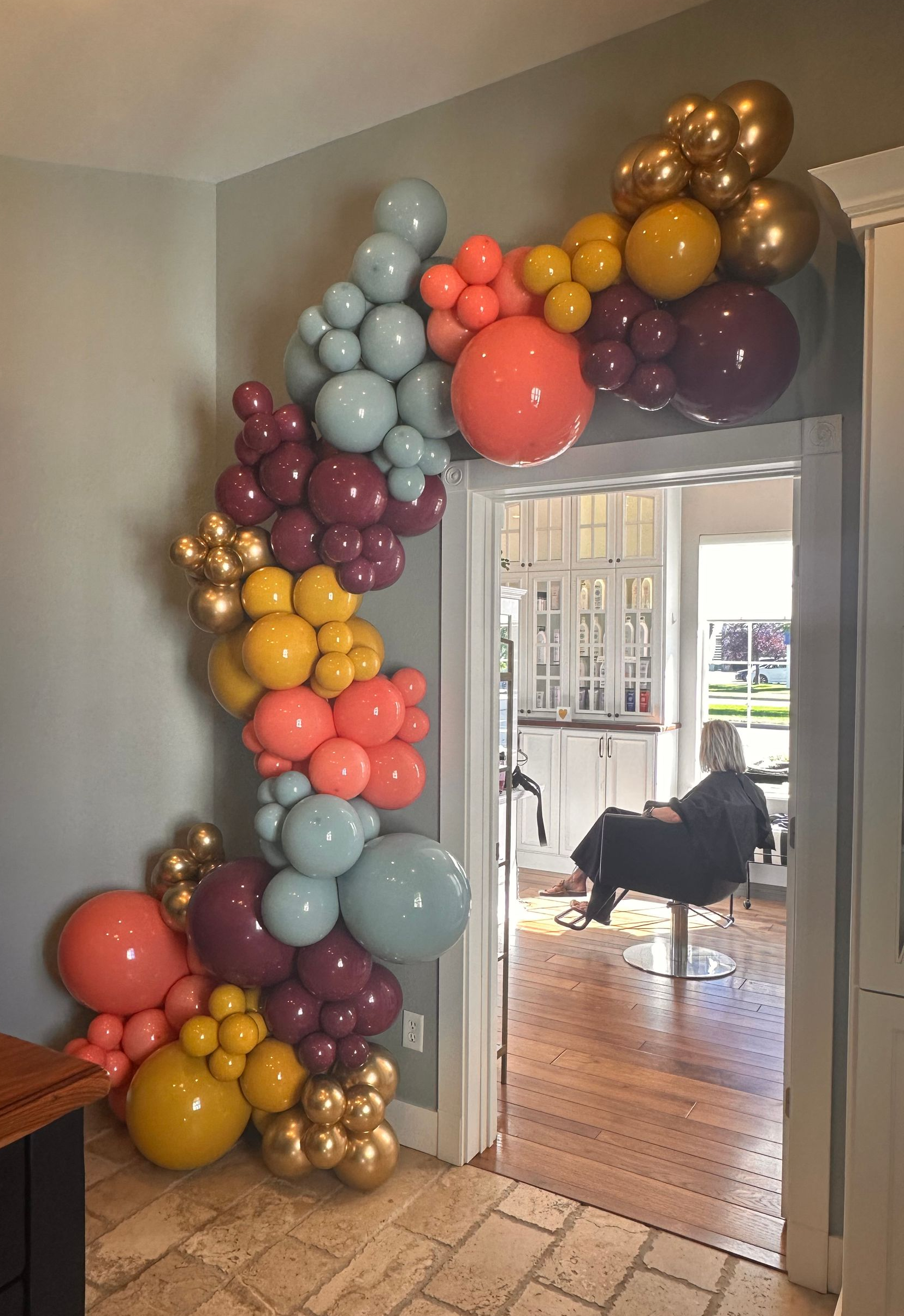 Balloon arch in teal, coral, gold, and maroon over a doorway.