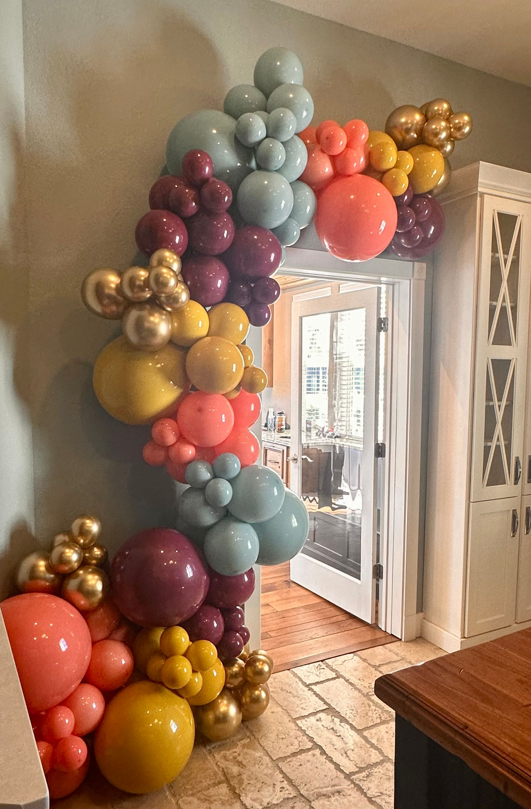 Balloon archway in various colors over a doorway, including pink, blue, gold, and burgundy balloons.
