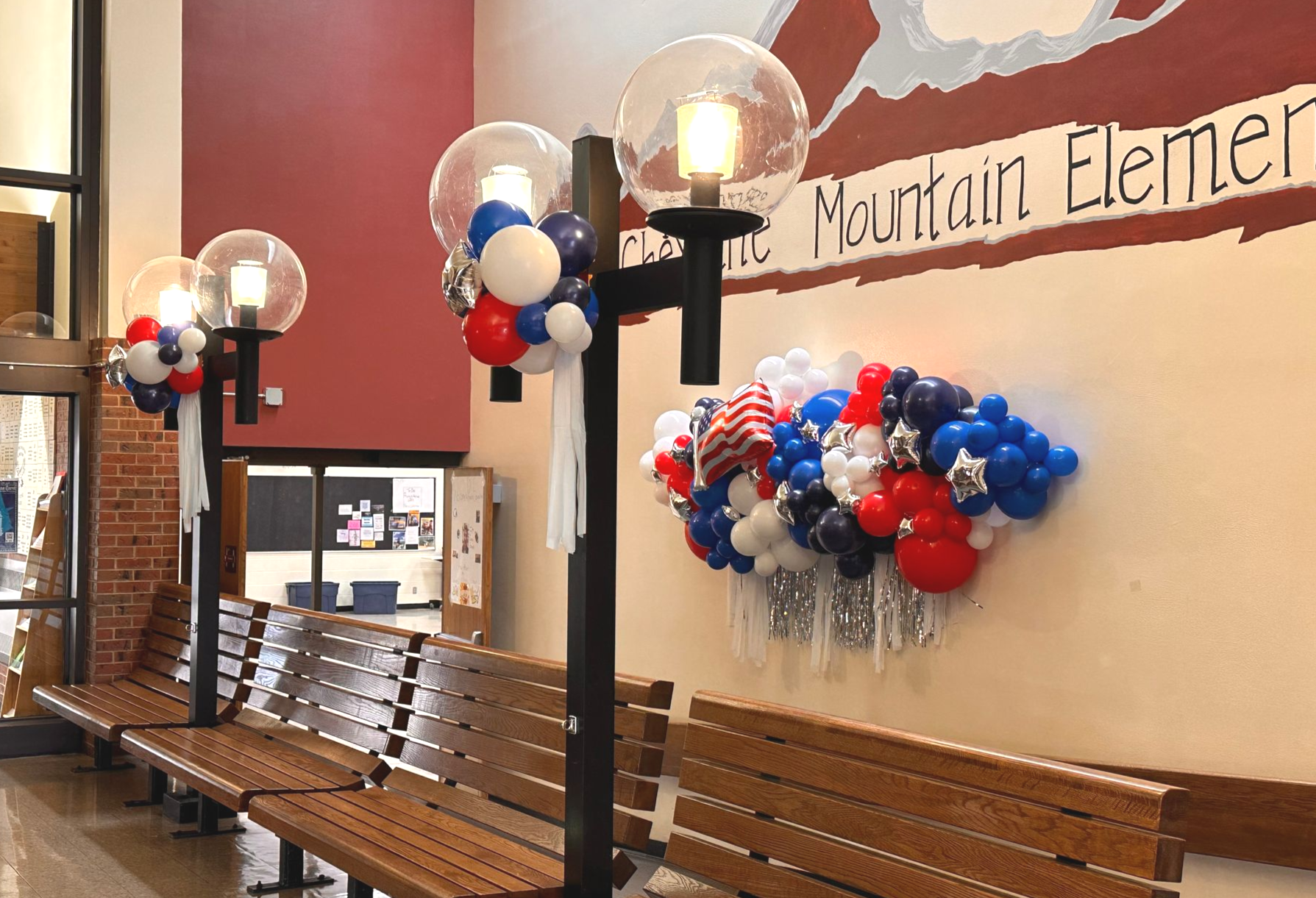 Hallway decorated with red, white, and blue balloons around light fixtures and against a wall. Benches in front.