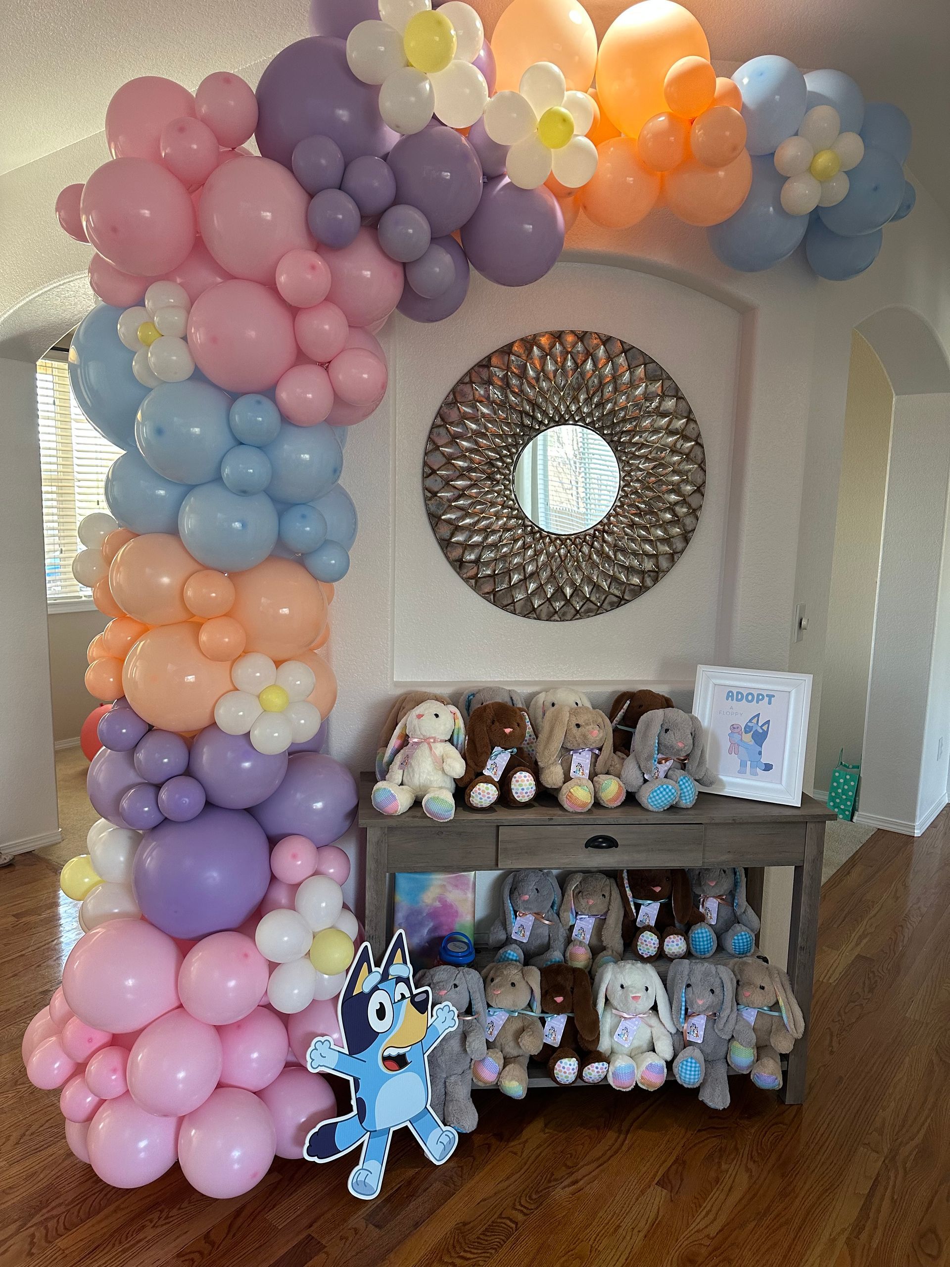Balloon arch with flowers and stuffed animals on a table. Bluey stands in front.