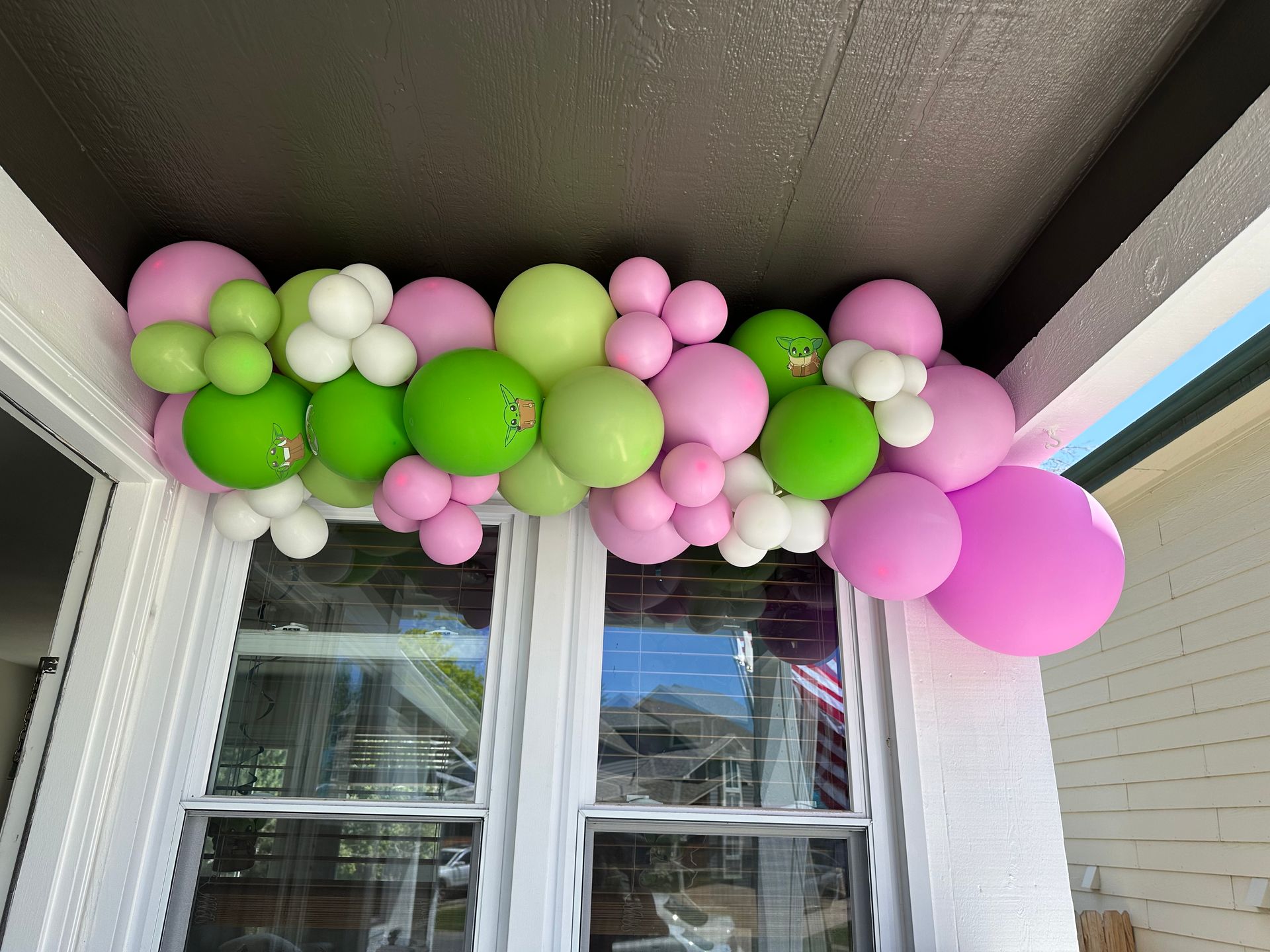 Pink, green, and white balloon garland above a window.