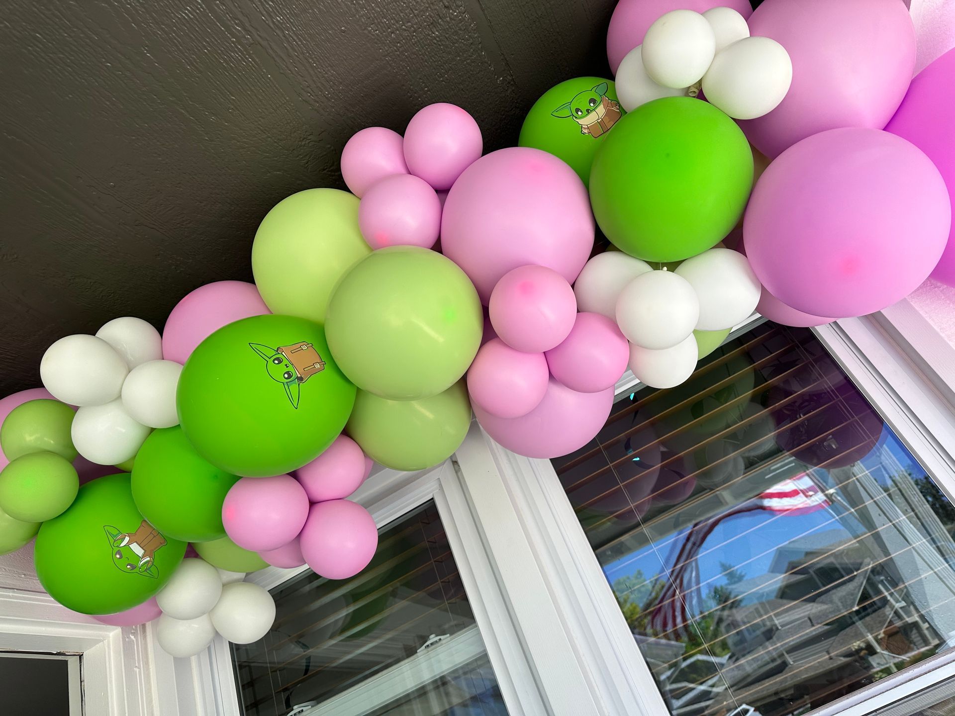 Balloon garland with white, light green, pink, and dark pink balloons, decorated on a window frame.