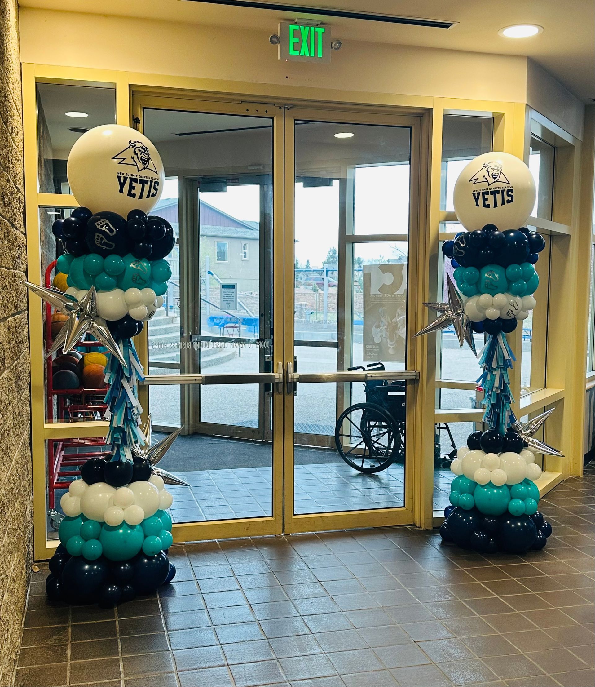 Two balloon columns flank double doors. Teal, black, and white balloons. Silver star accents. 