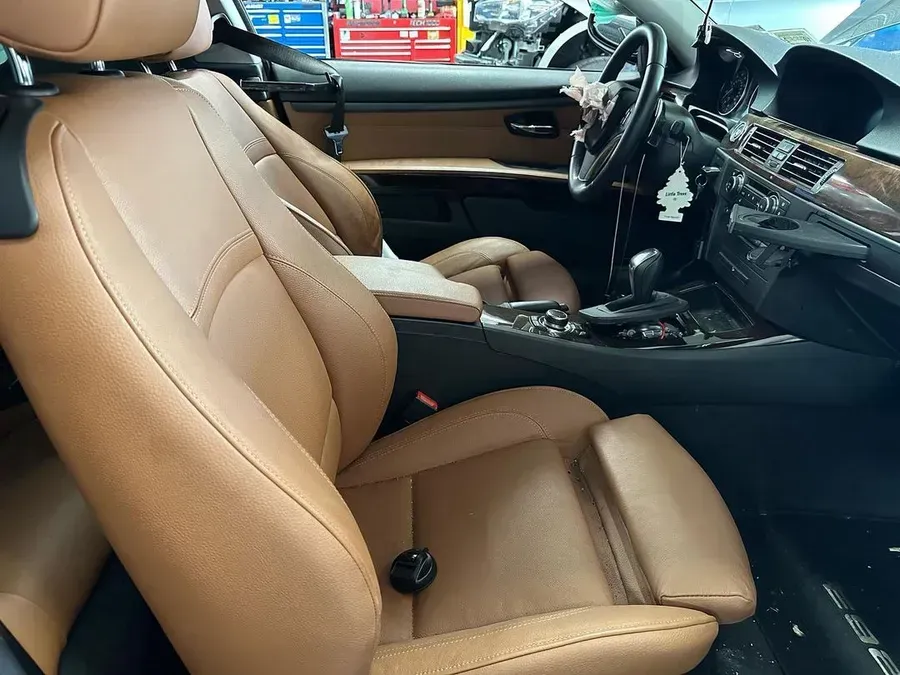 Tan leather car interior, focused on the driver's seat. Steering wheel, dashboard, and gear shift are visible.