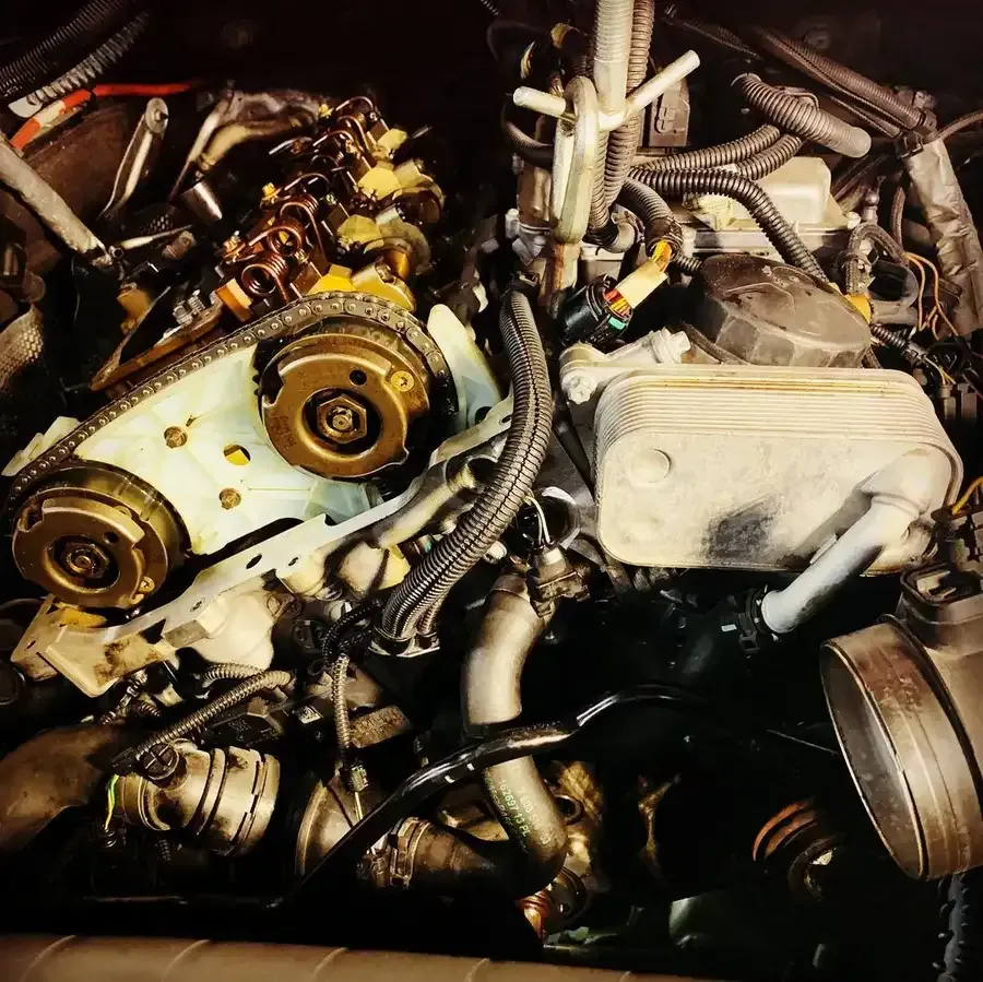 Car engine partially disassembled, showing timing chain, oil cooler, and hoses.