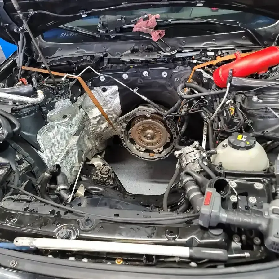 Car engine bay partially disassembled for repair. Components, tools, and wires visible.
