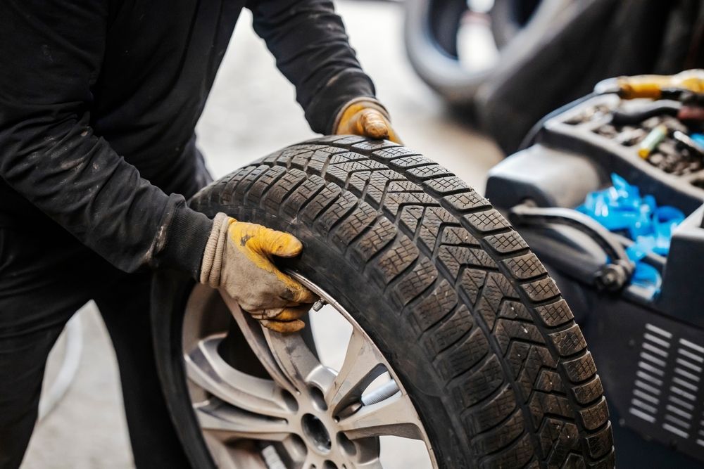 Mechanic in gloves holding a tire with silver wheel. Tire shop setting.