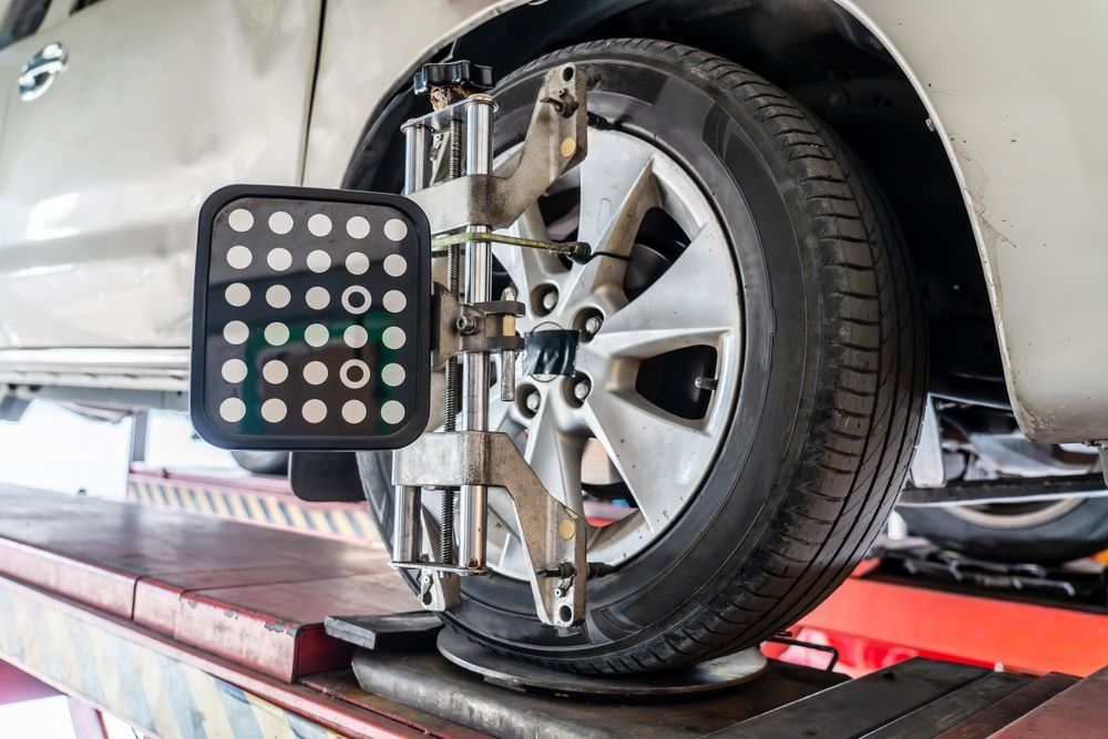 Car wheel being aligned with a machine on a lift, tires are black, the car is white.