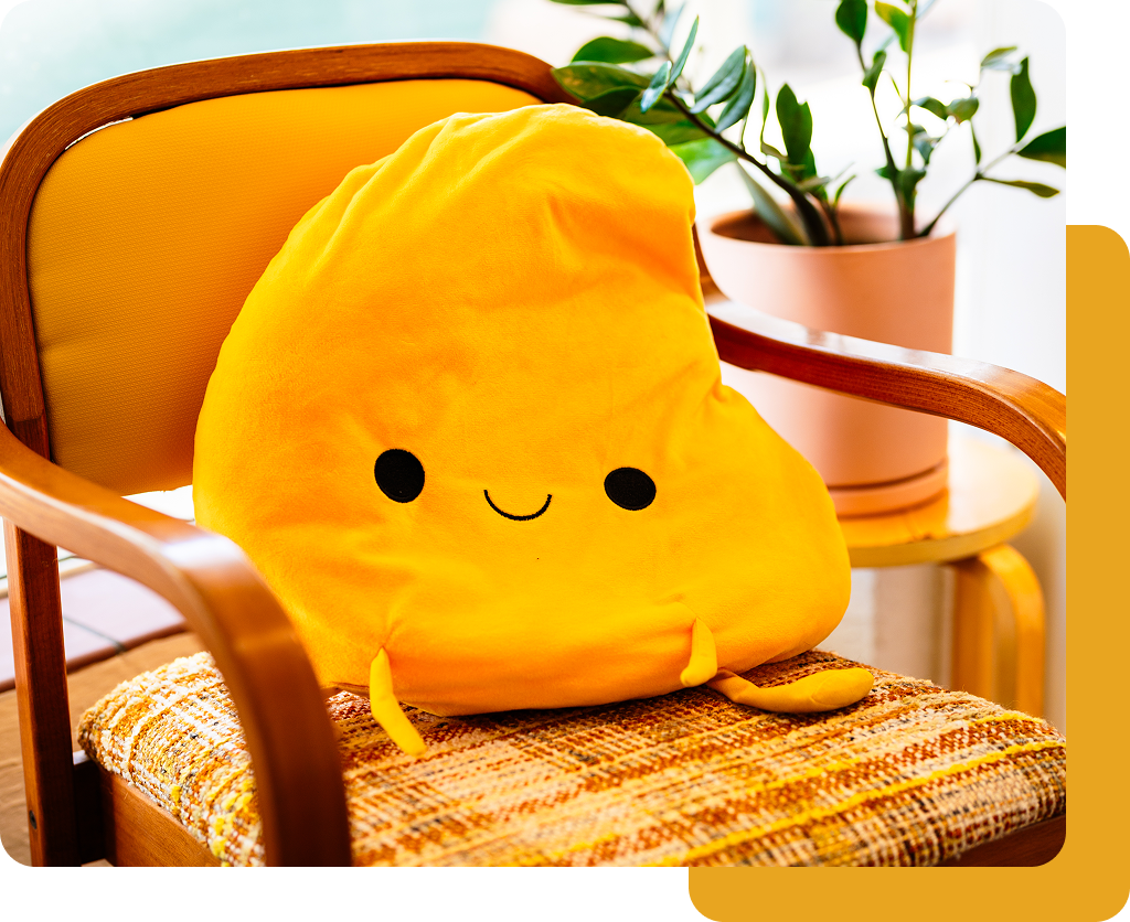 Smiling yellow plush pillow on a wicker chair beside a potted plant