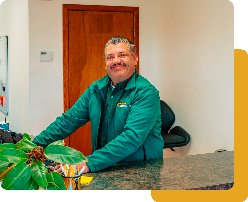 Man in a green shirt leaning on a counter in an office, smiling near a wooden door.
