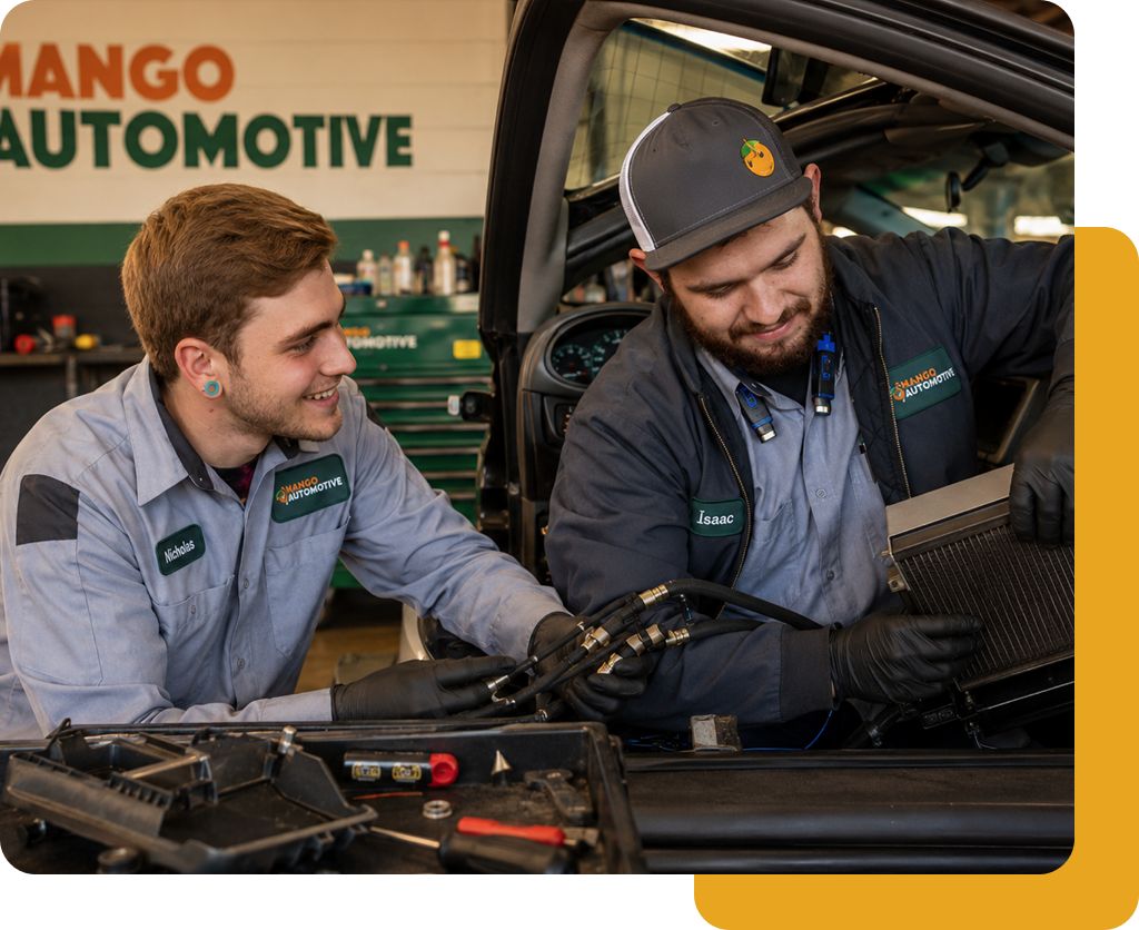 Two mechanics in gray uniforms inspecting a car engine in a garage with Mango Automotive signage