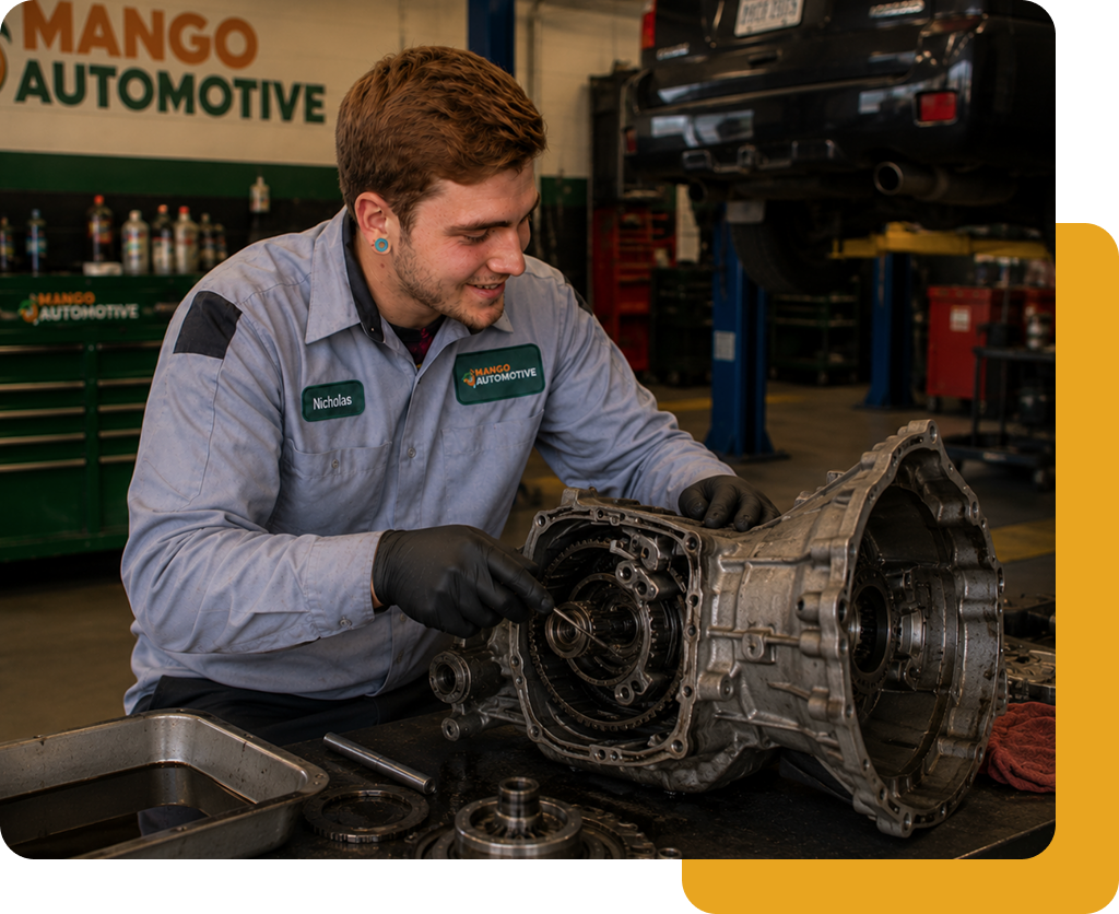 Mechanic in gray uniform working on a car transmission in a garage workshop