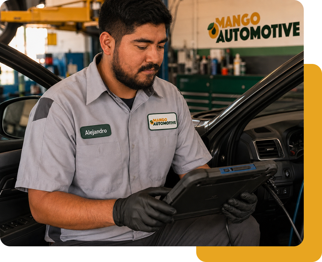 Mechanic in gray uniform using a tablet beside a car in a Mango Automotive garage