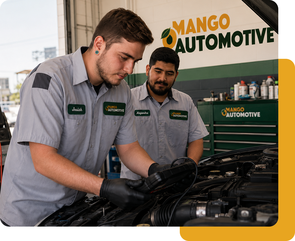 Two mechanics in gray uniforms working on a car engine at Mango Automotive shop