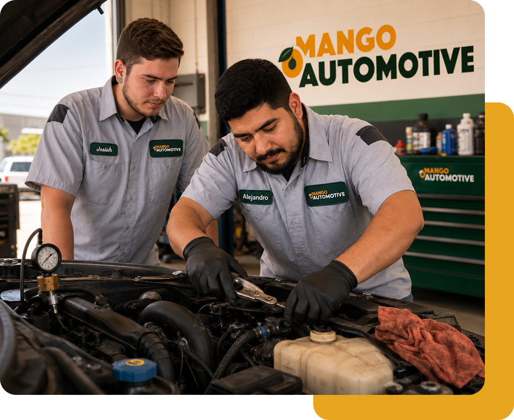 Two mechanics in gray uniforms inspect a car engine in a Mango Automotive workshop.