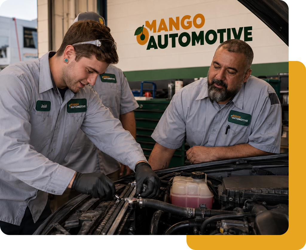 Two mechanics in gray uniforms inspect engine components at Mango Automotive shop.