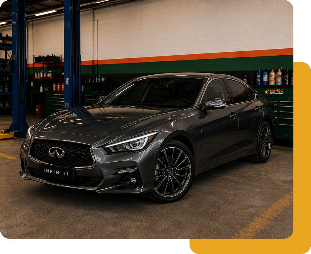 Dark gray Infiniti sedan in an auto shop, parked under a lift with bright green and orange wall stripes