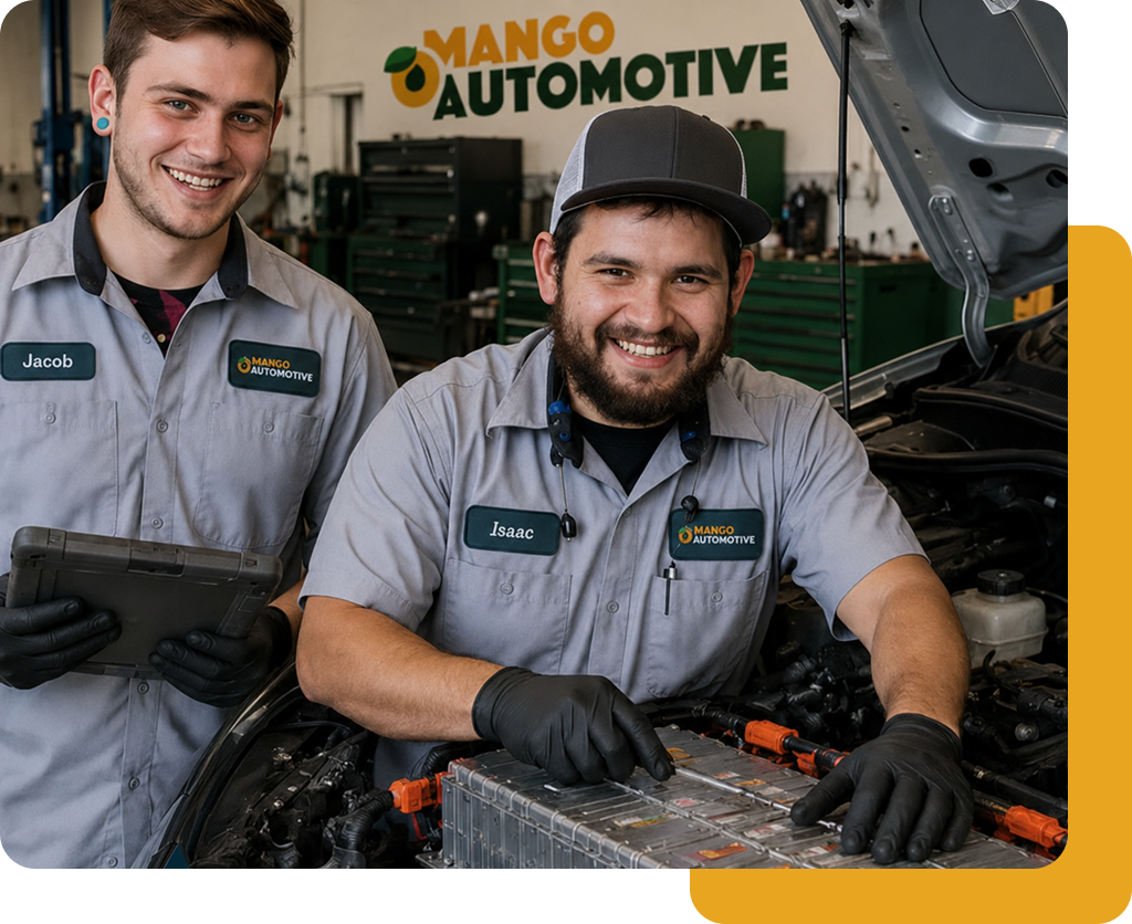 Two mechanics in gray uniforms smiling in an auto shop beside a car engine and Mango Automotive sign