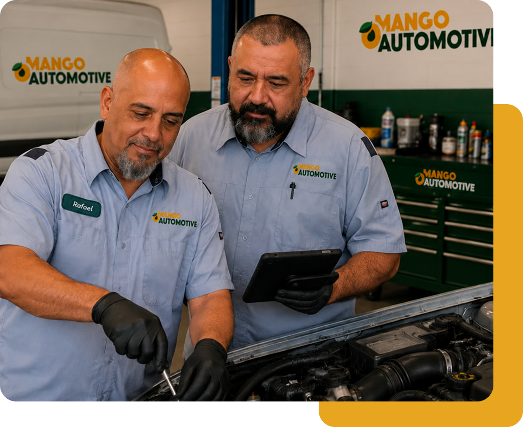 Two mechanics in light blue uniforms inspect a car engine at Mango Automotive shop.