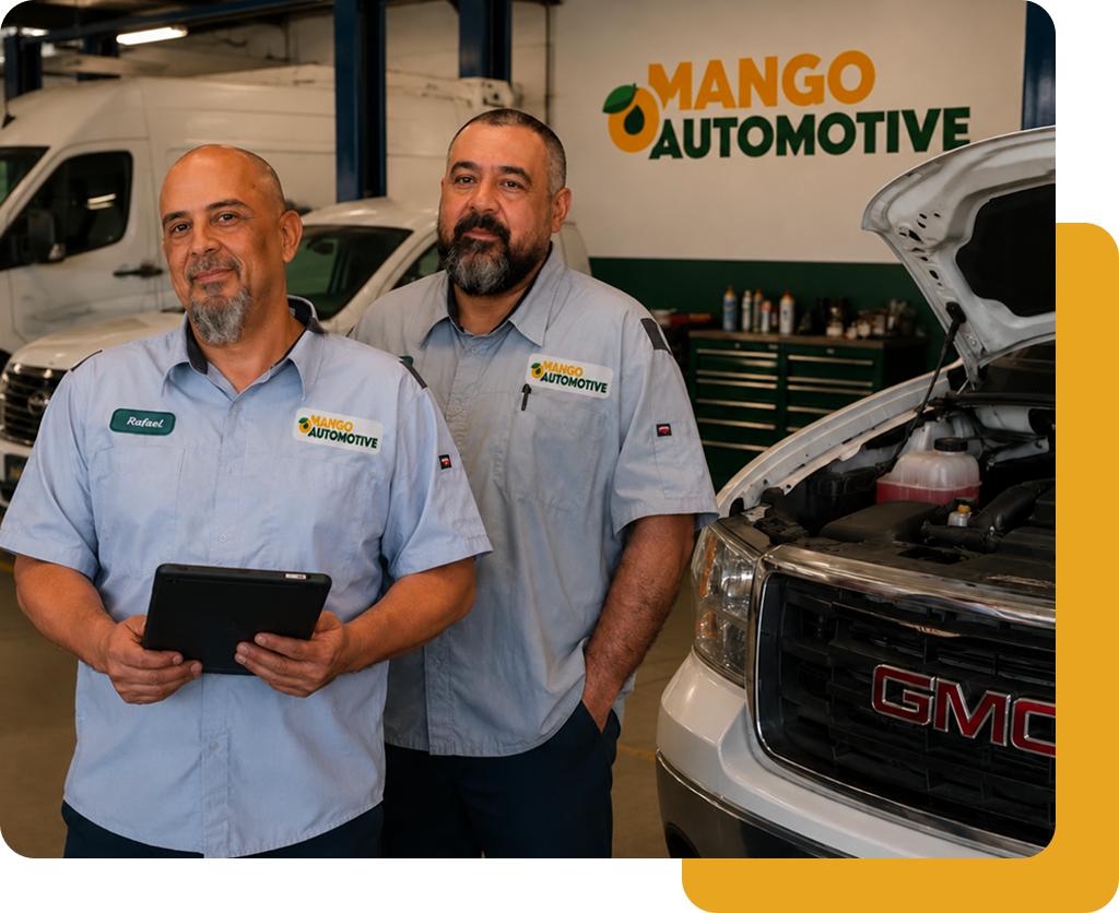 Two mechanics in light blue shirts standing in a Mango Automotive shop beside a GMC truck with hood open