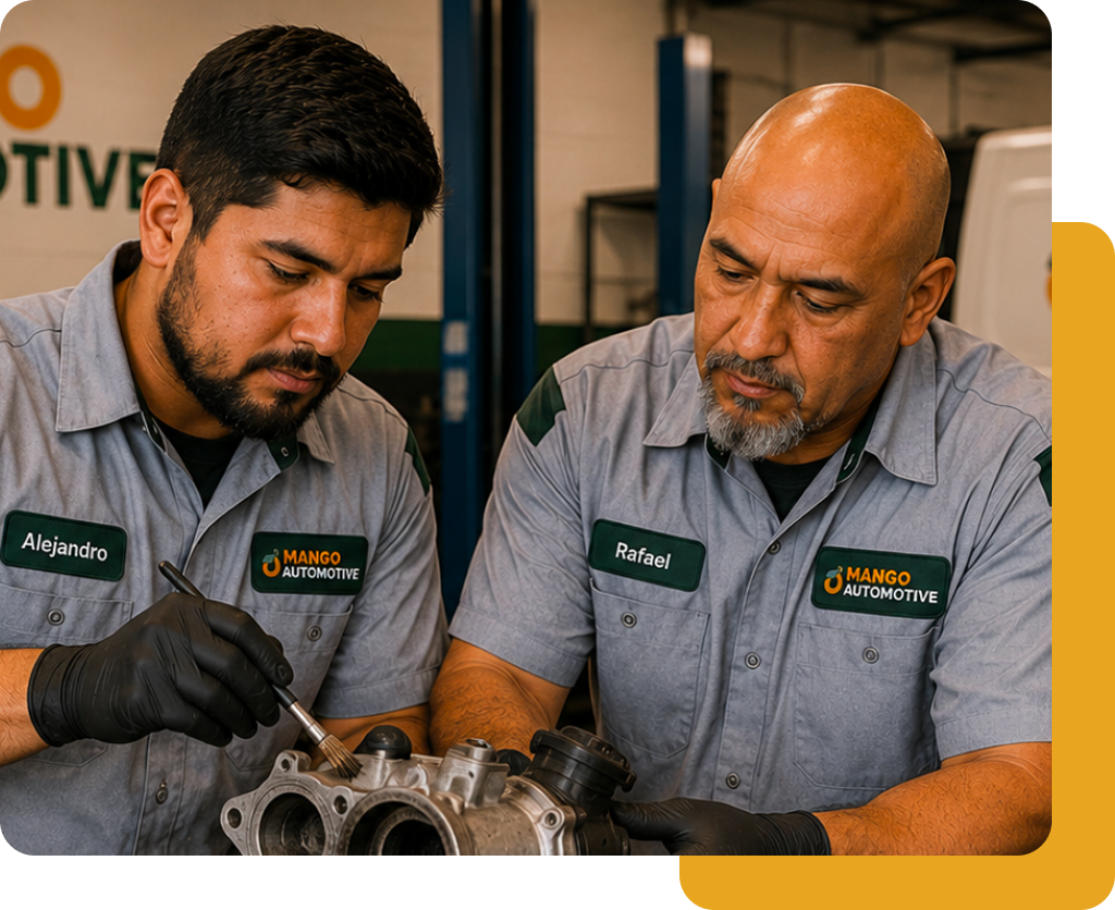 Two mechanics in gray uniforms inspecting an engine part in a workshop