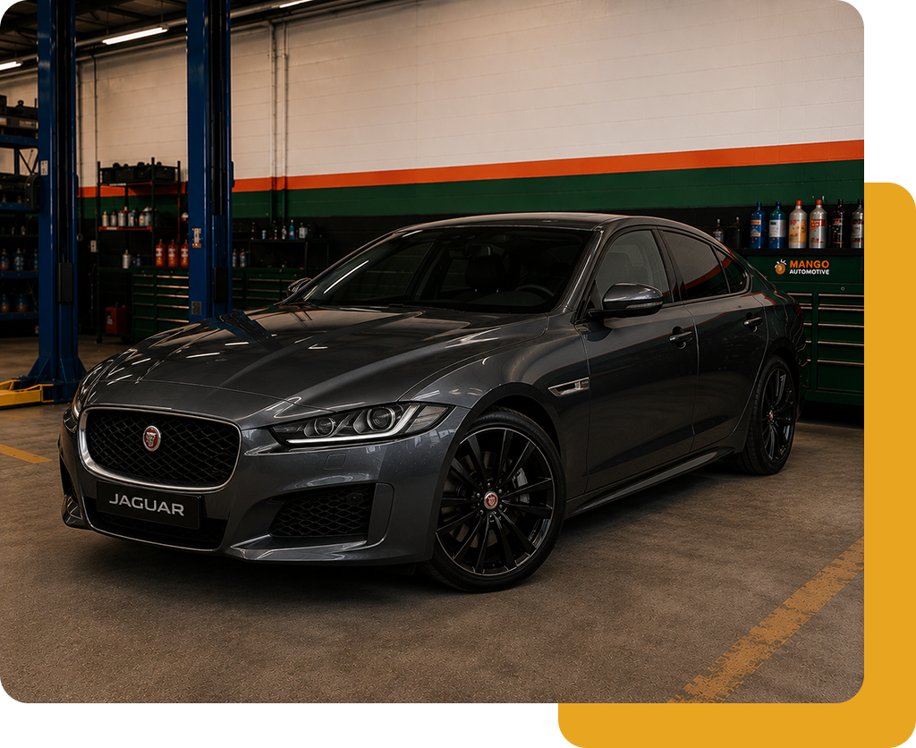 Dark gray Jaguar sedan parked indoors in a garage or showroom with orange and green wall stripes.