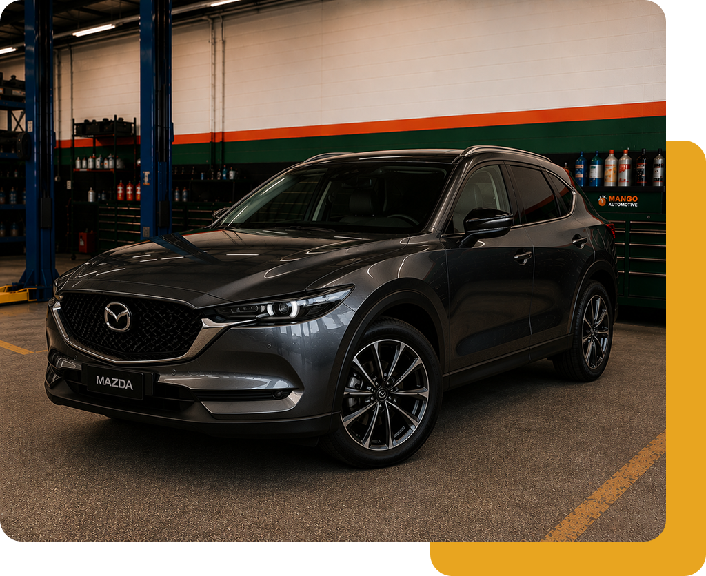 Dark gray Mazda SUV parked indoors in a garage, front three-quarter view, with orange and green wall stripes.