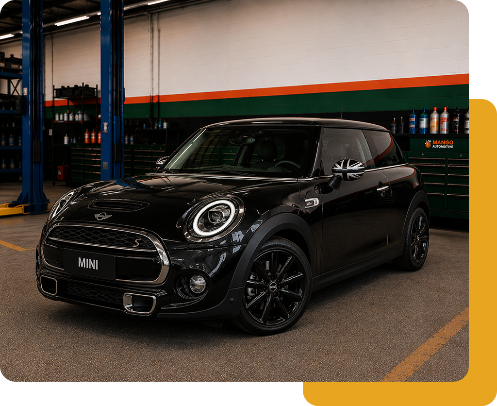 Black Mini Cooper in a workshop, parked near a lift with blue and orange walls.
