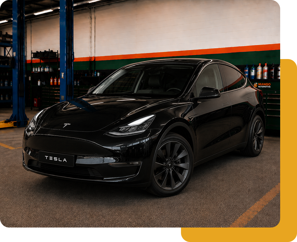 Black Tesla Model Y parked in a garage, front-left view with a white and orange wall behind it