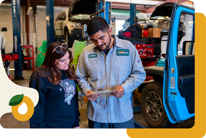 Two mechanics inspect parts beside a blue vehicle in a workshop