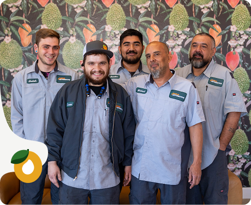 Five coworkers in light gray uniforms stand smiling in front of a leafy patterned wall.