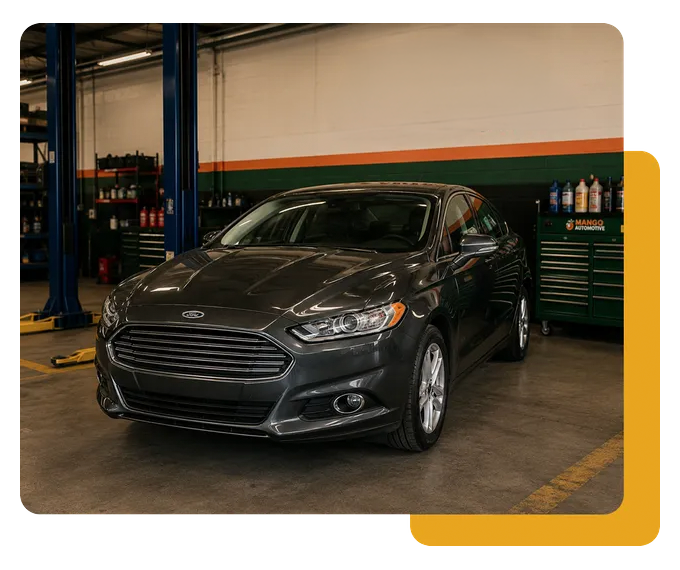 Dark gray sedan parked in an auto shop bay with a lift and tool cabinets in the background