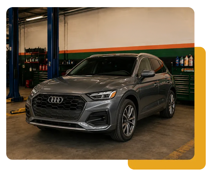 Gray Audi SUV in an auto shop garage, parked indoors beside tools and lift equipment.